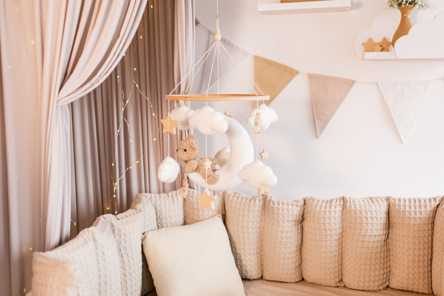 Decorative mobile with teddy bear and plush moon hanging above a sofa in a nursery.