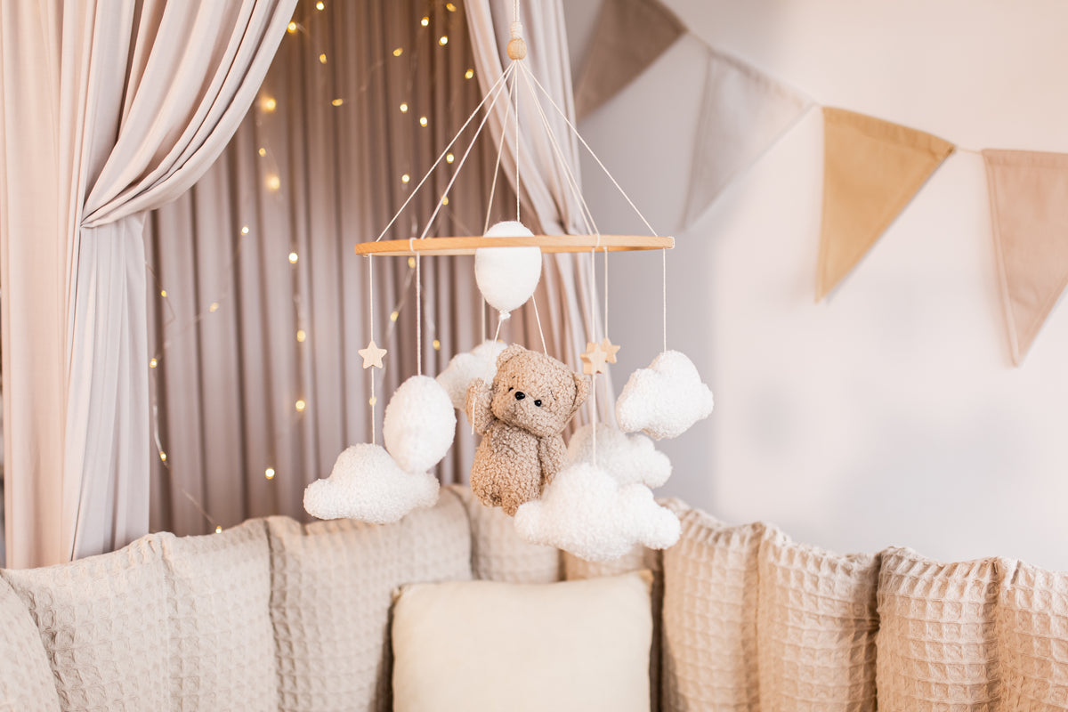 Baby mobile with teddy bear hanging above a crib in a nursery.