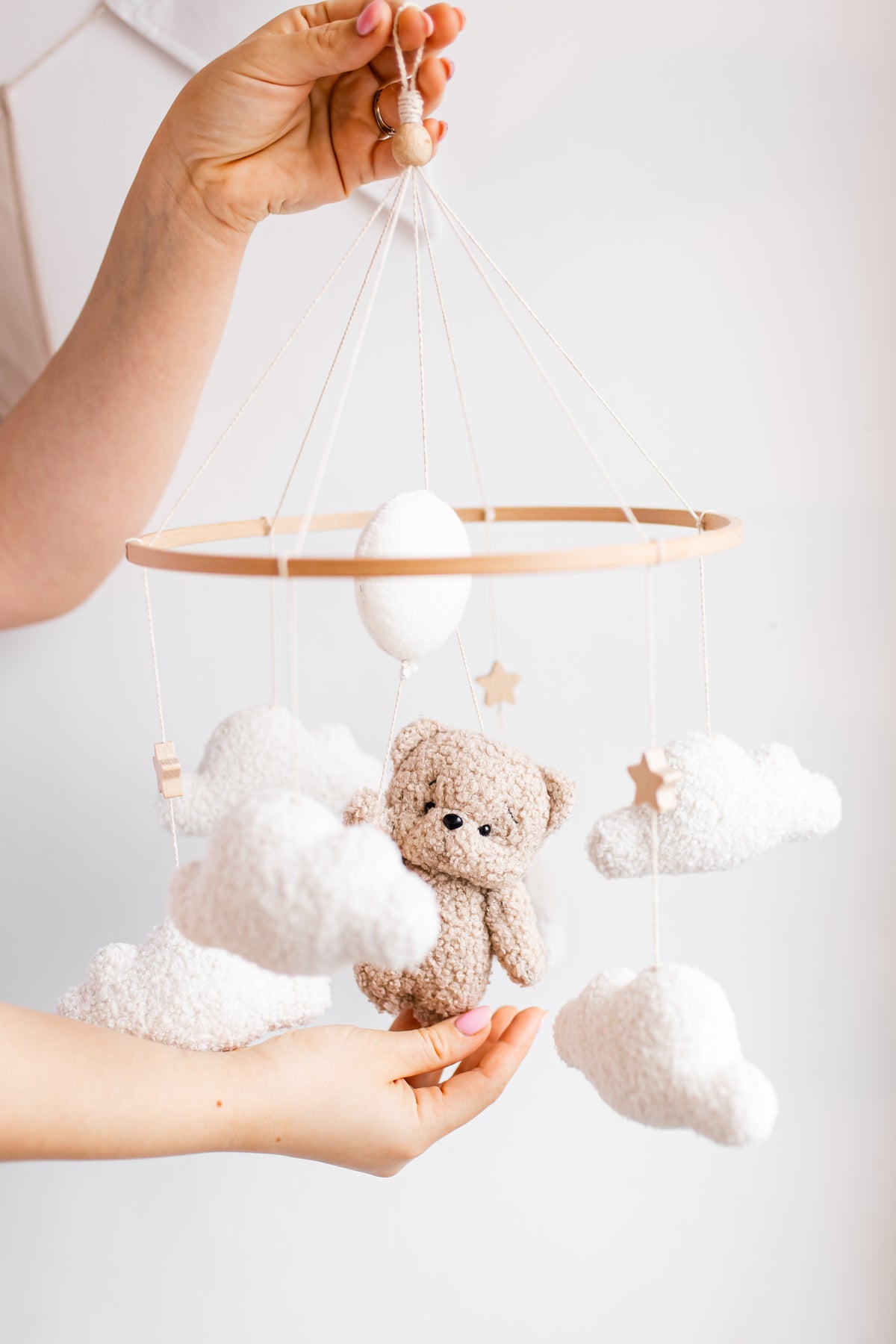 Baby mobile with teddy bear and clouds held by a person against a white background