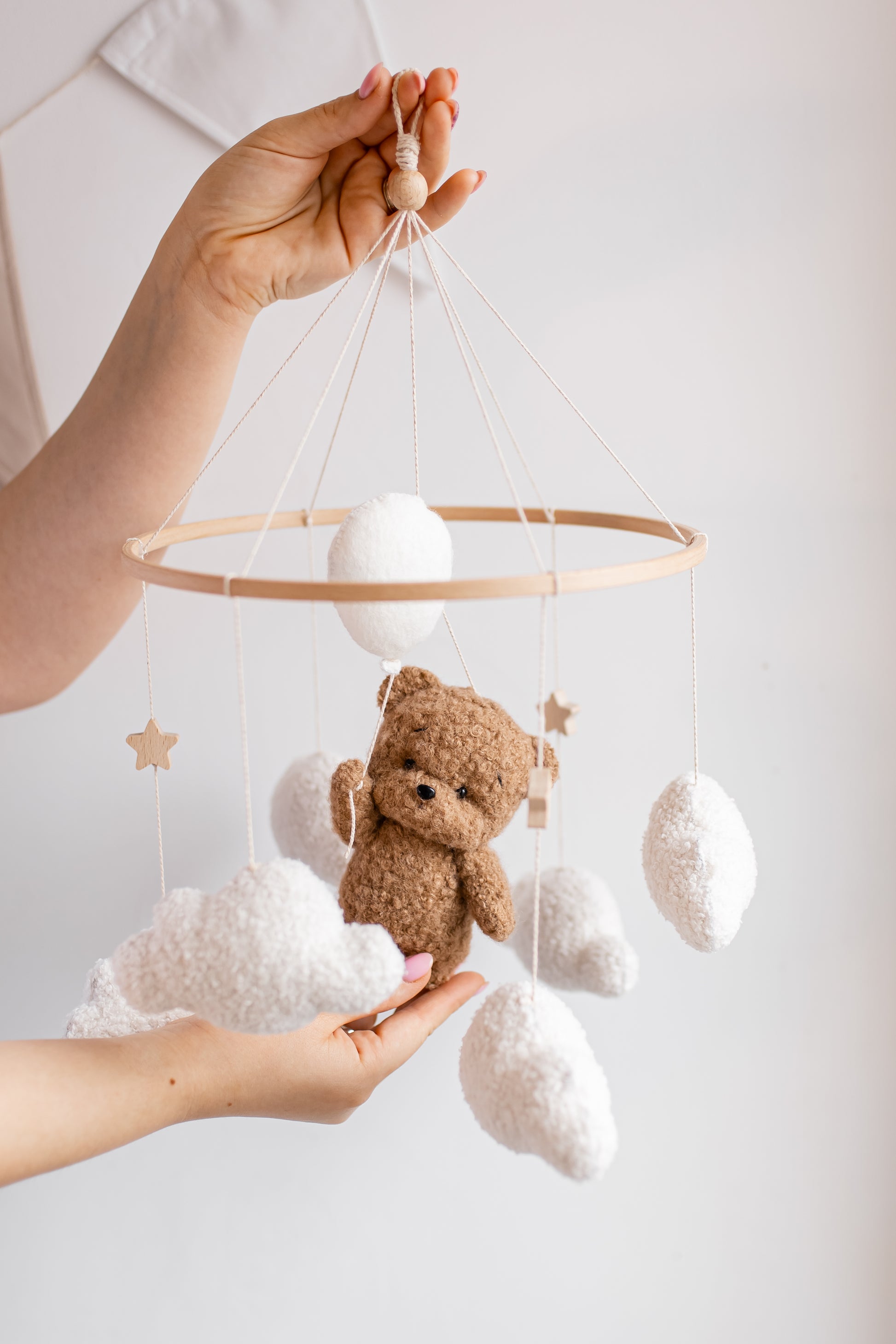 Hand holding a baby mobile with a teddy bear and stars against a light background