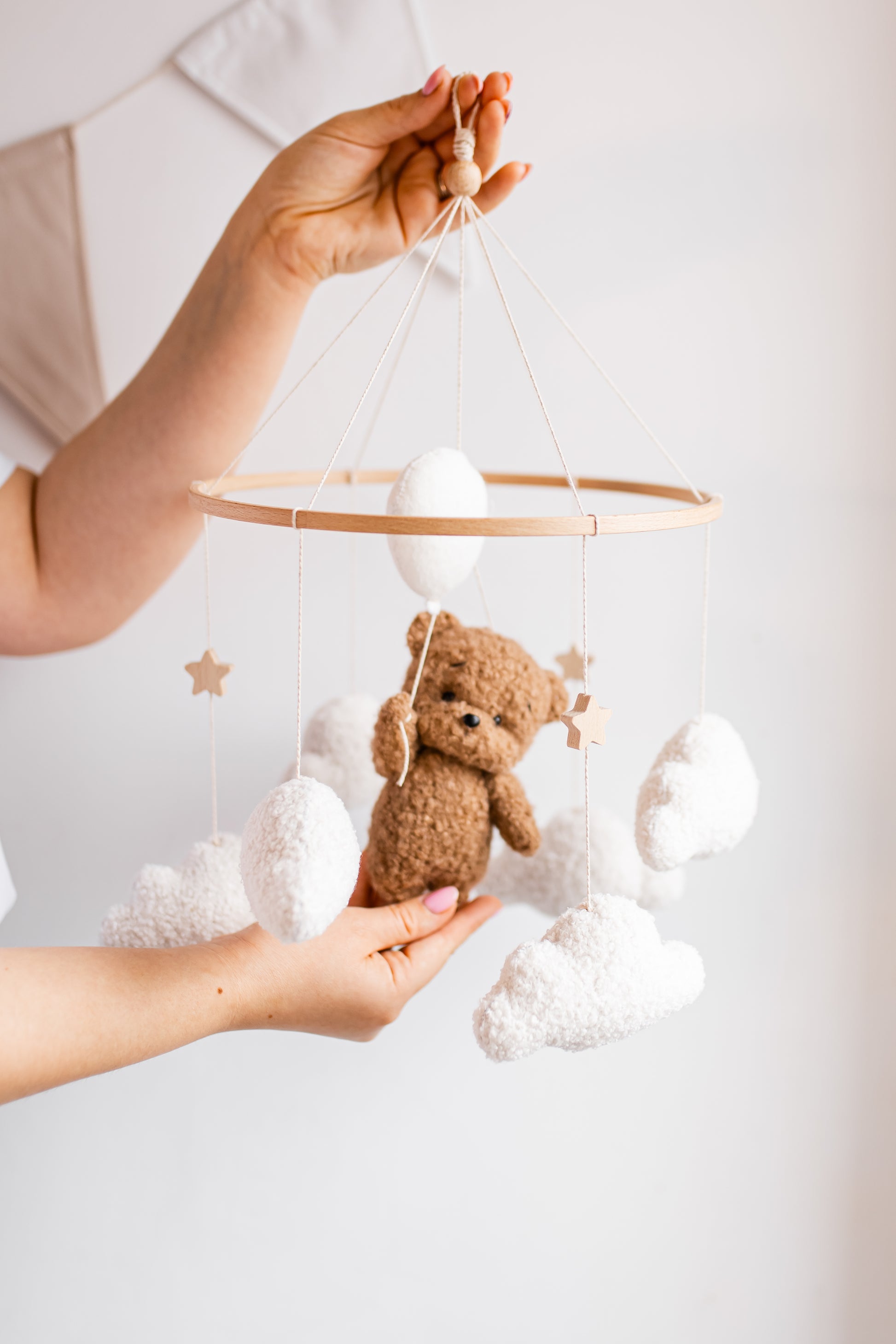Baby mobile with teddy bear and clouds held by a hand against a light background