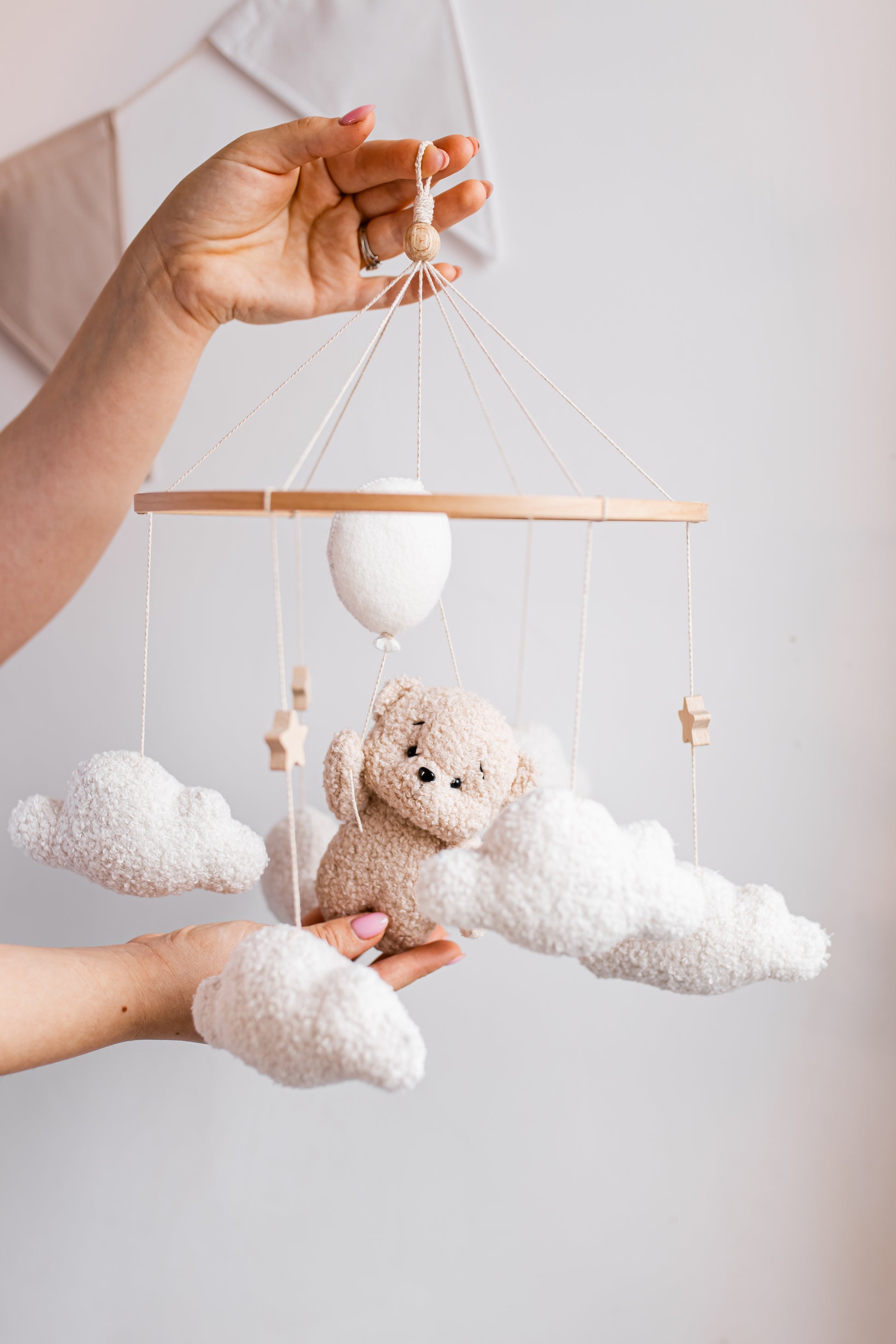 Hand holding a baby mobile with teddy bear, cloud, and star decorations against a plain background