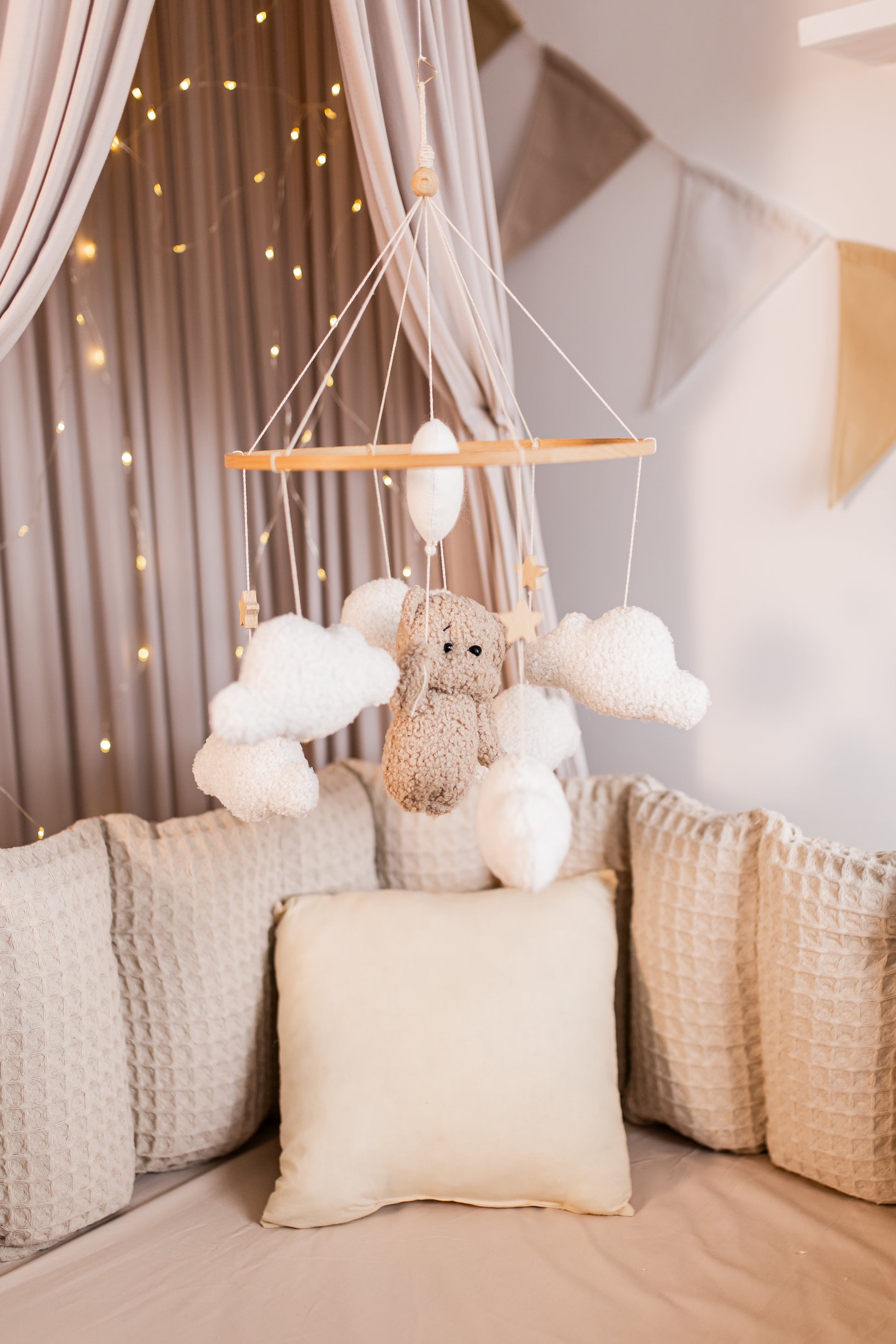 Children's room with a teddy bear and cloud mobile hanging above a bed.
