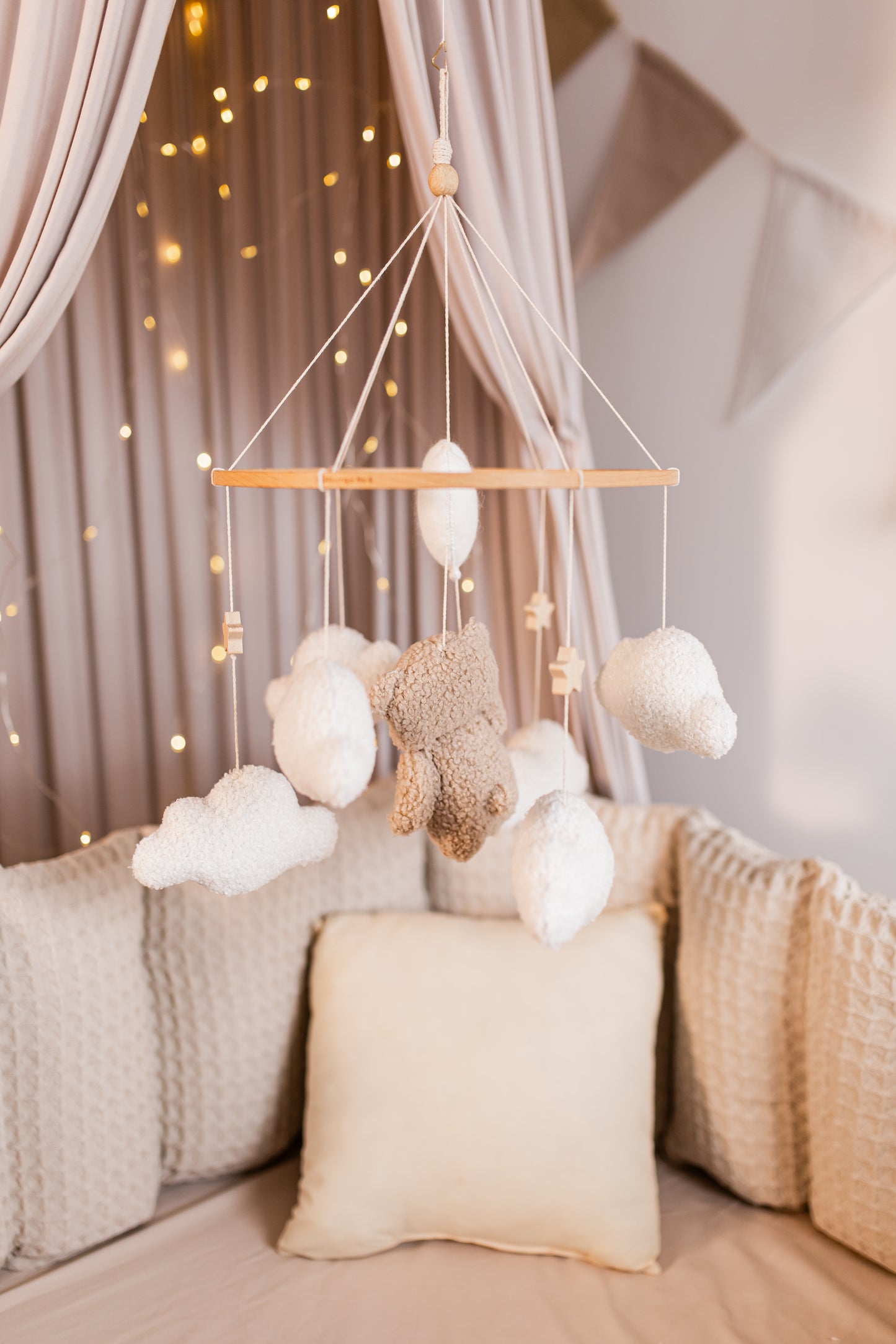 Decorative mobile with clouds and teddy bear hanging above a bed with soft lighting.