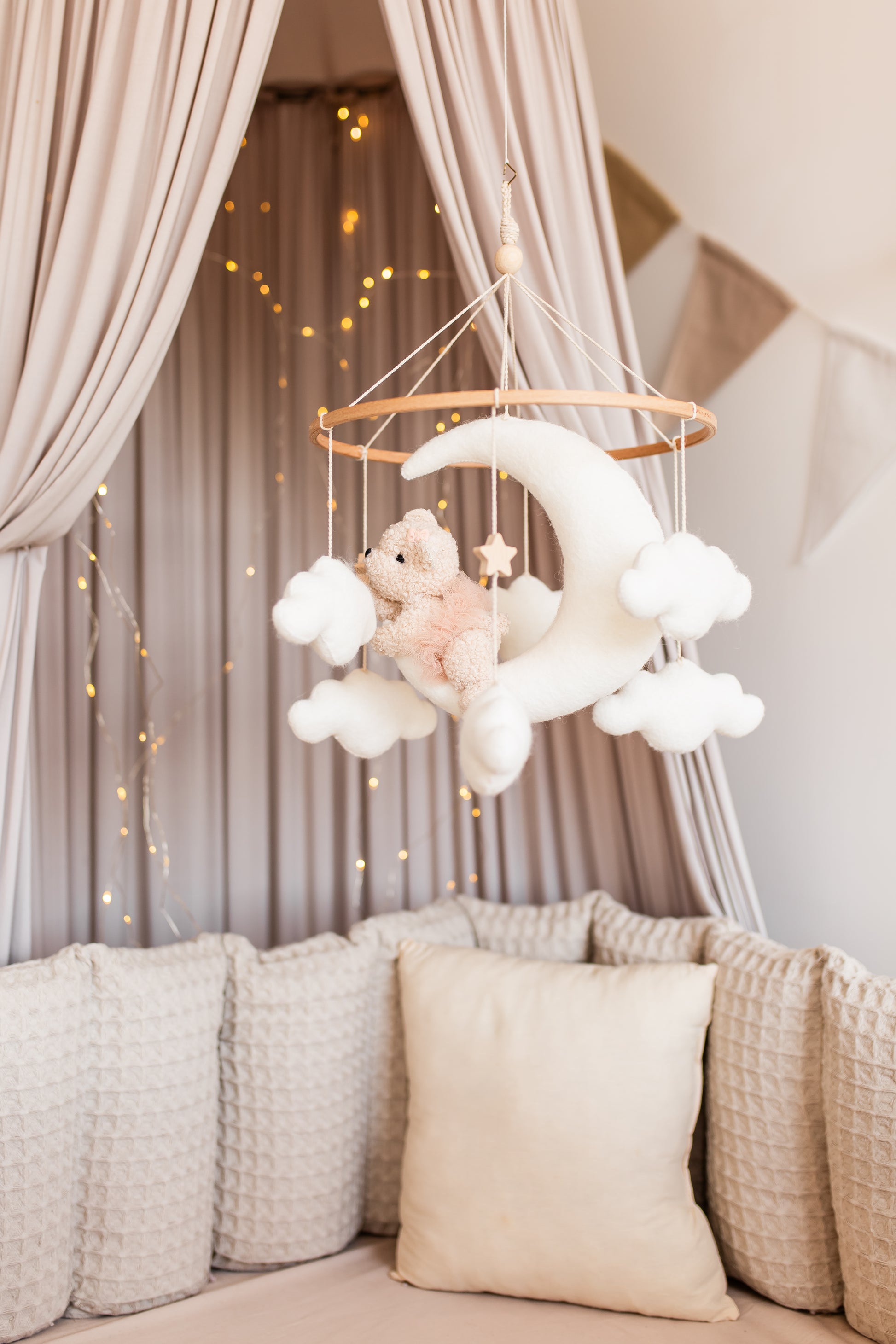 Decorative baby mobile with clouds and teddy bear hanging above a crib with soft bedding.