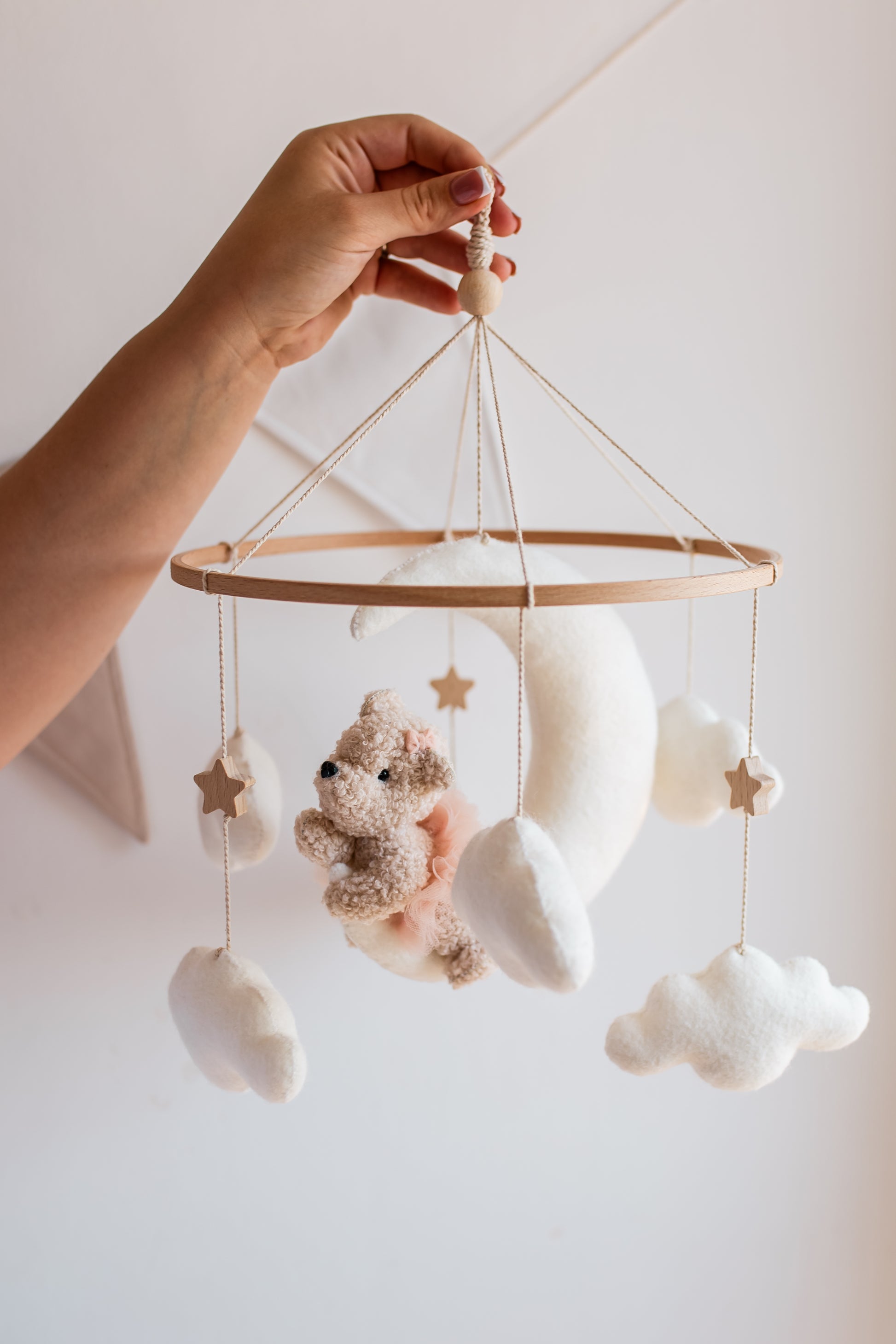 Baby mobile with teddy bear, stars, and clouds hanging from a string against a light background.