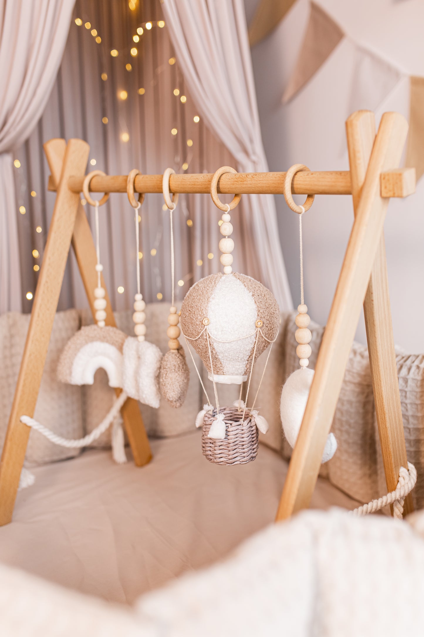Wooden crib with hanging baby gym featuring a hot air balloon design, surrounded by soft textures and lighting.