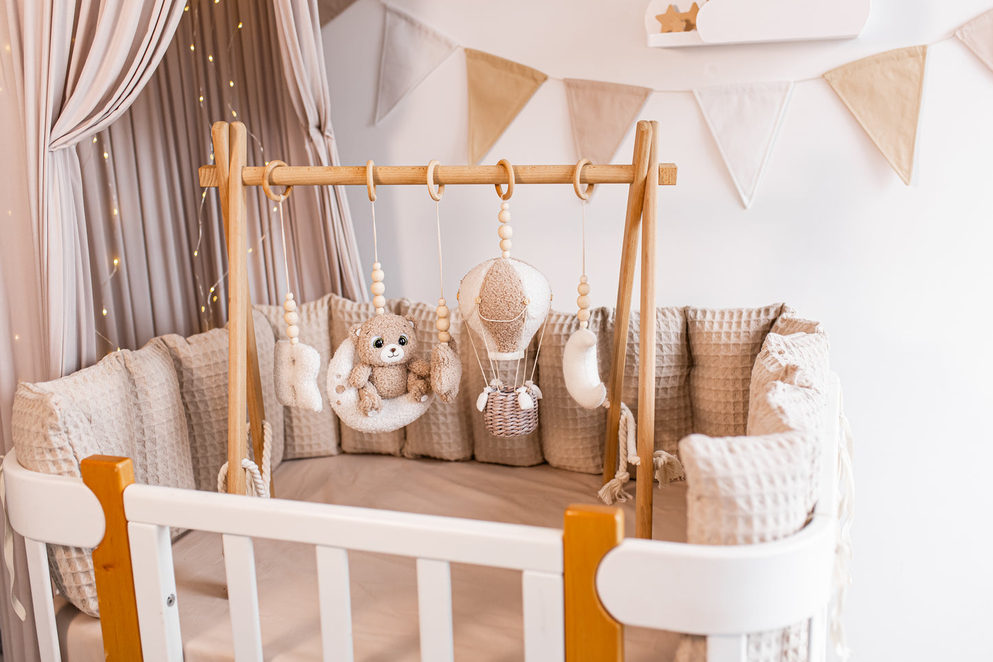 Baby crib with wooden canopy, pillows, and hanging toys baby gym in a nursery setting.