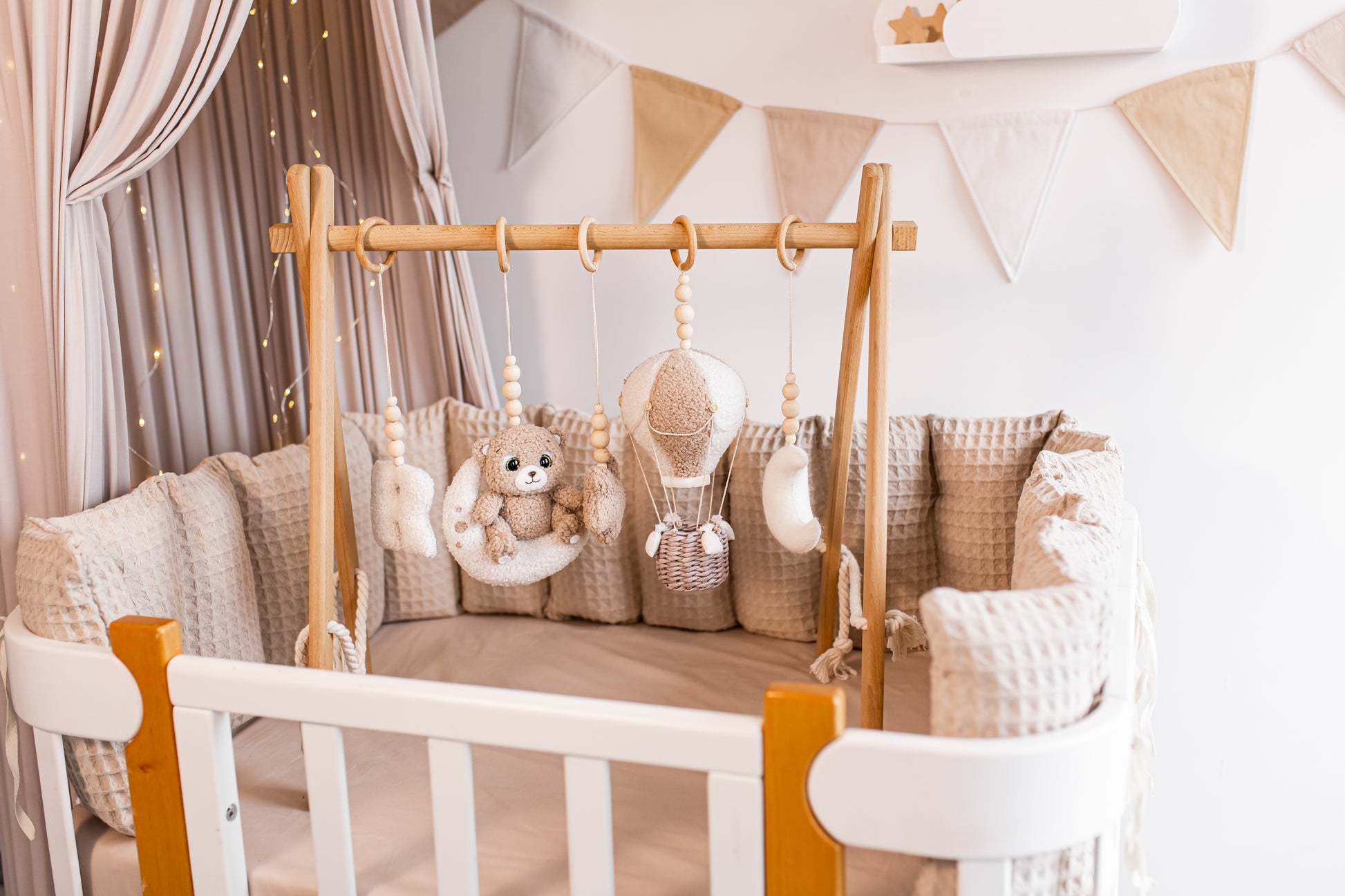 Baby crib with wooden canopy, pillows, and hanging toys baby gym in a nursery setting.