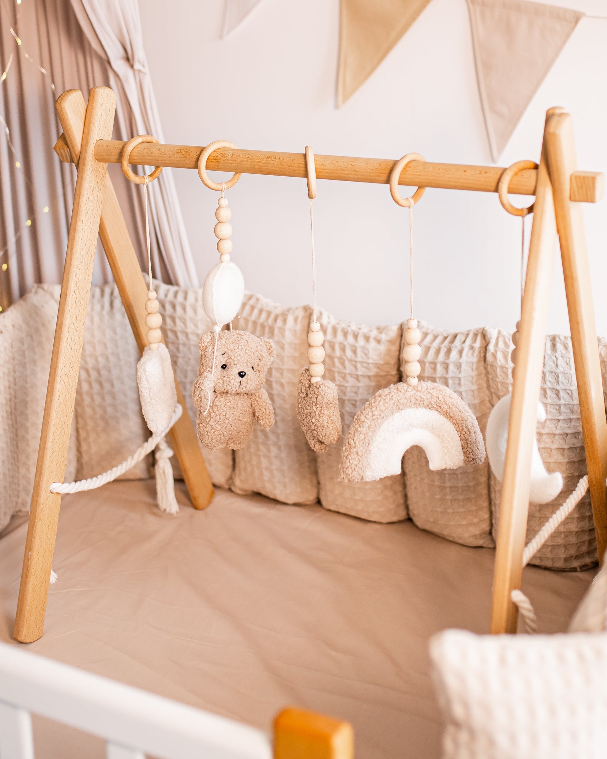 Nursery setup with wooden crib, play gym, teddy bear, and decorative elements.