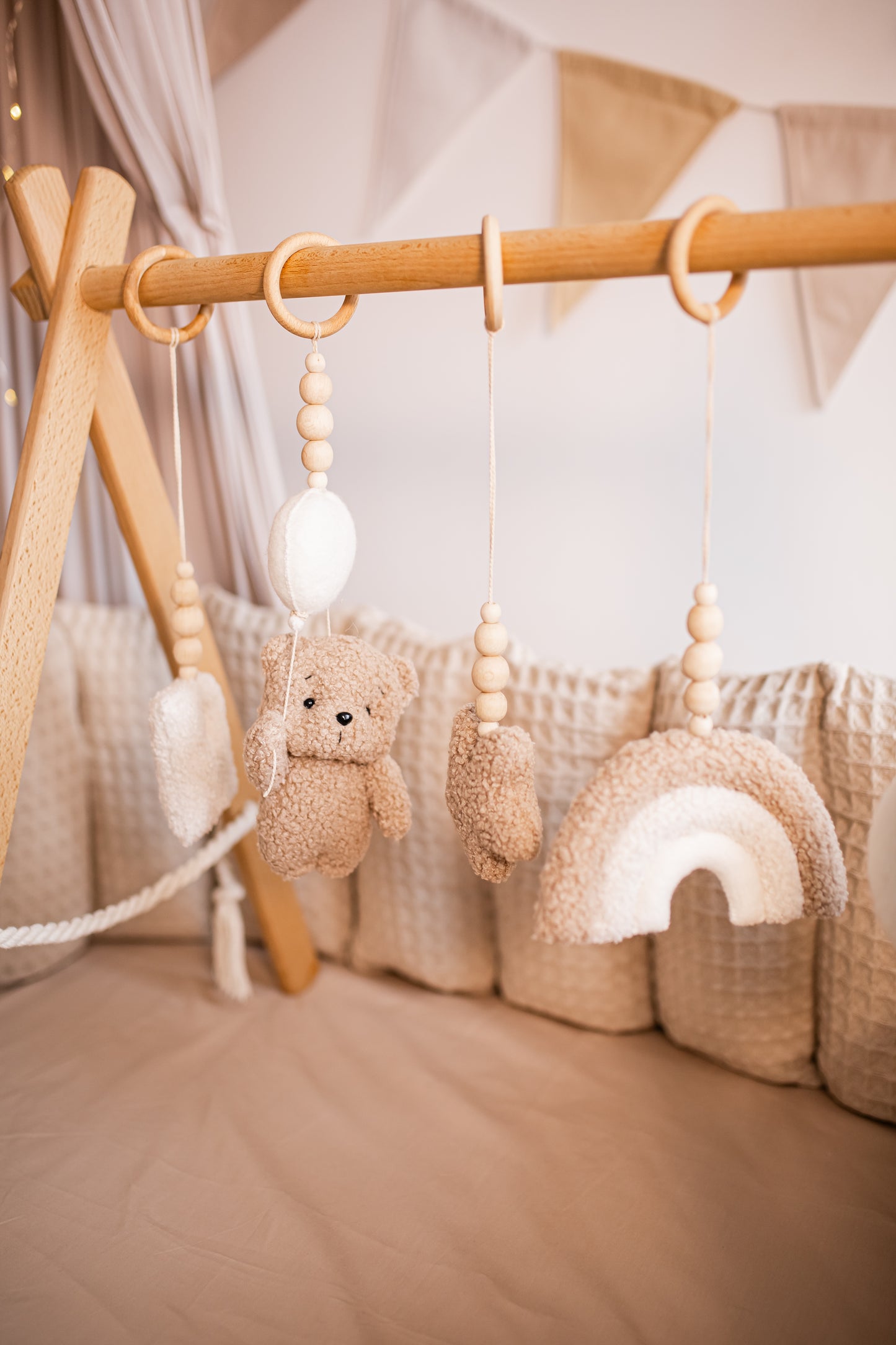 Baby crib mobile with teddy bear, play baby gym, cloud, and rainbow hanging from a wooden bar.