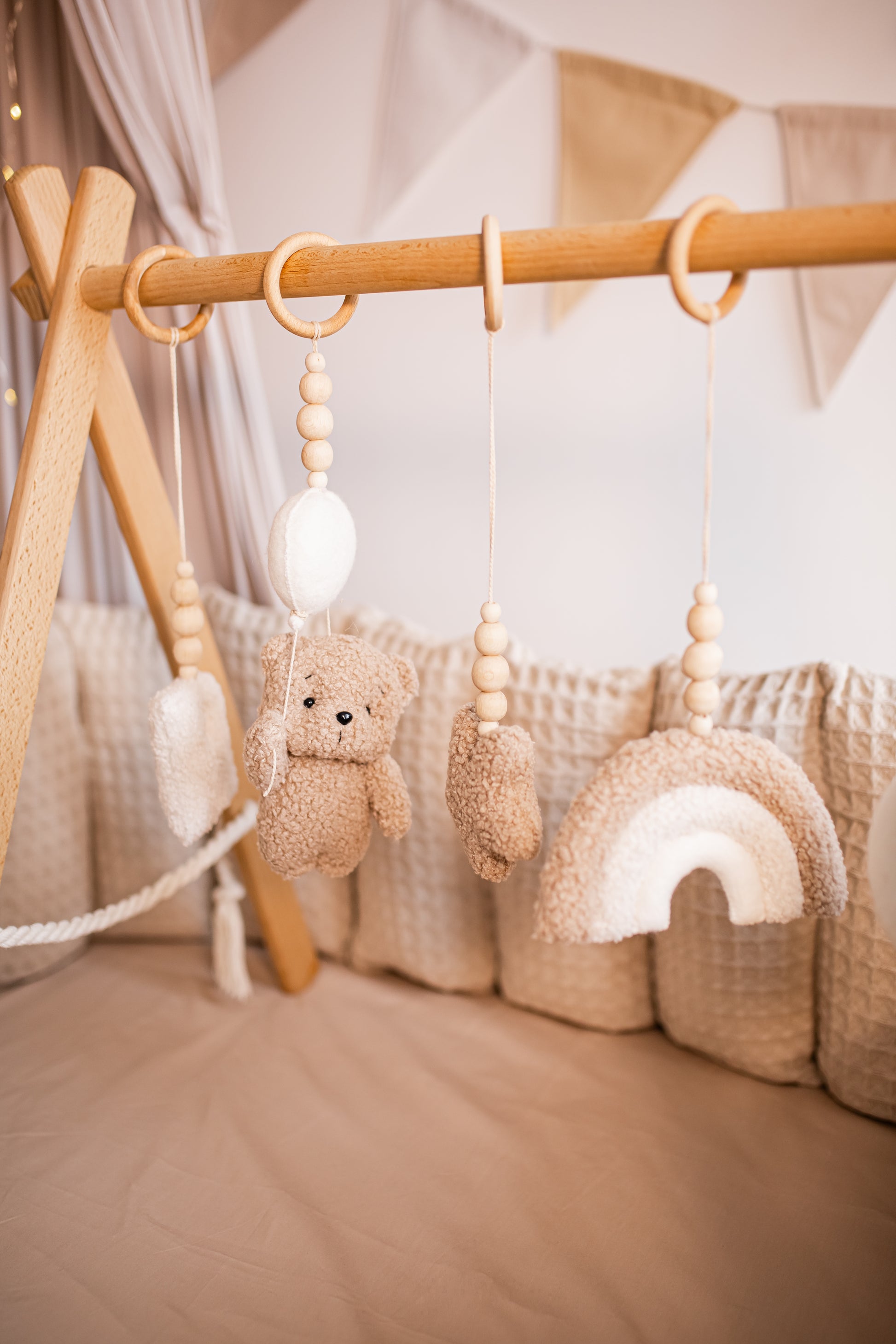 Baby crib mobile with teddy bear, play baby gym, cloud, and rainbow hanging from a wooden bar.