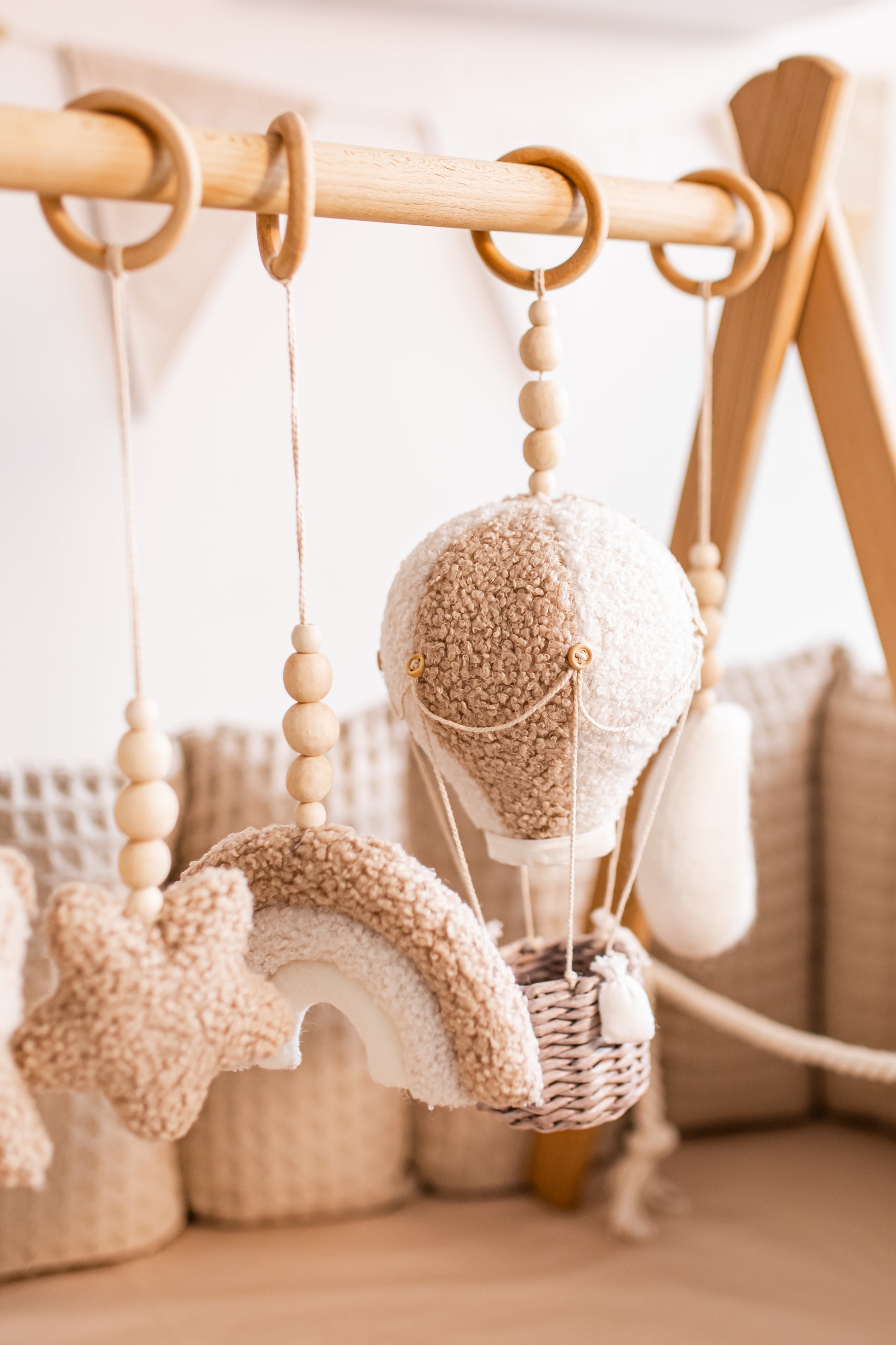 Decorative baby gym with hanging elements on a wooden rod against a neutral background