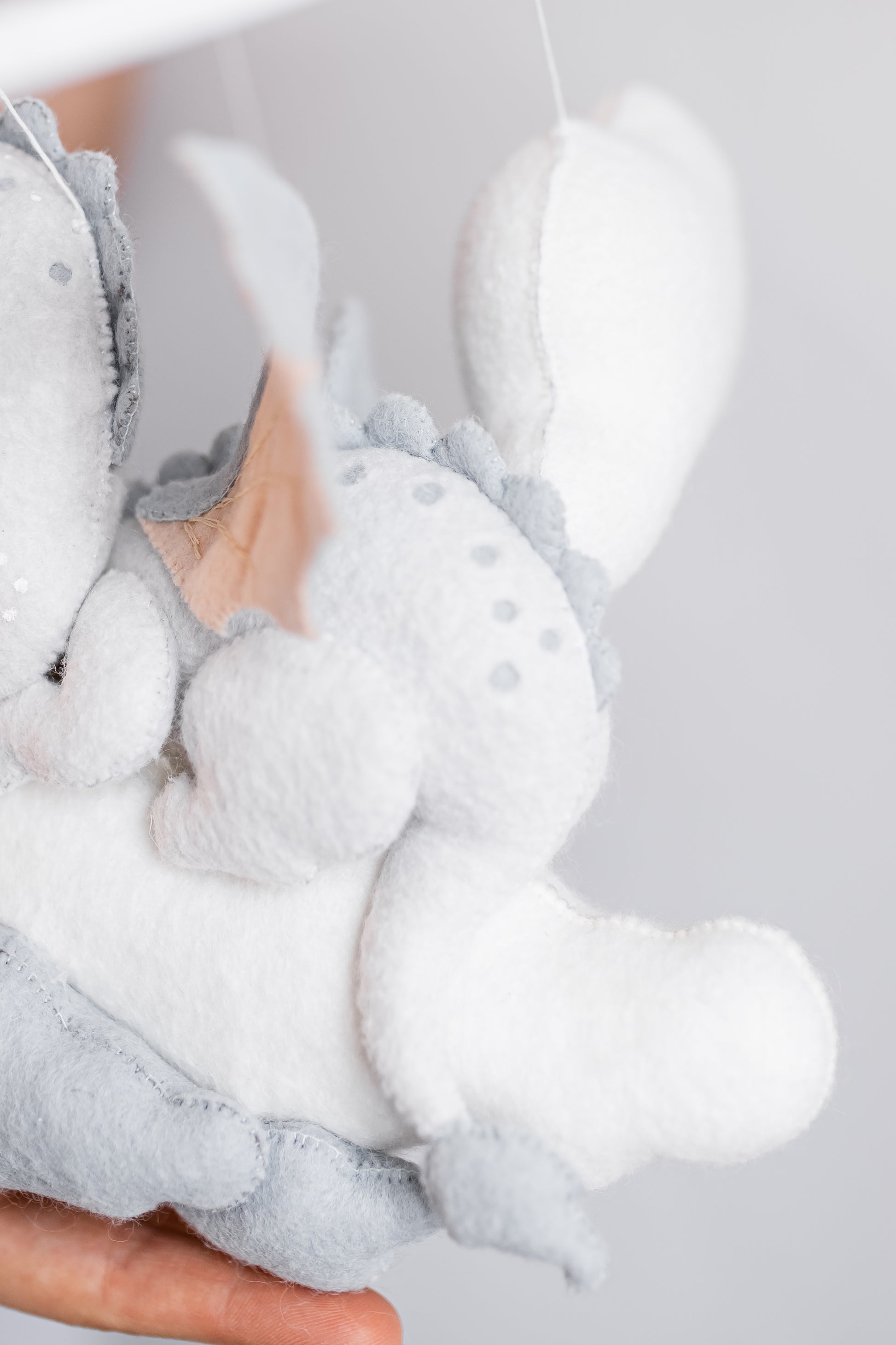 Gray plush dragon baby mobile held by a person against a light gray background