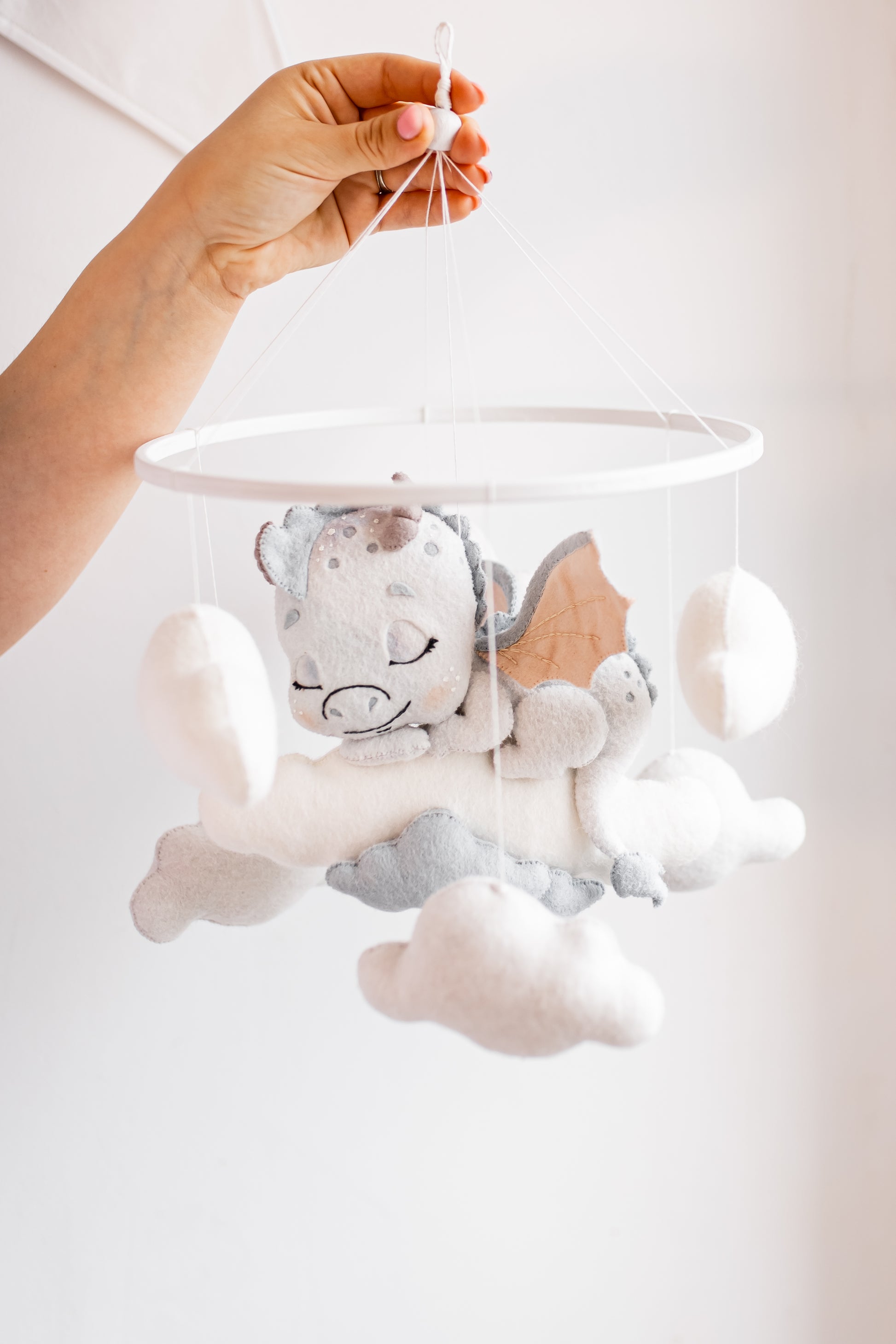 Baby mobile with baby dragon design held by a hand against a white background