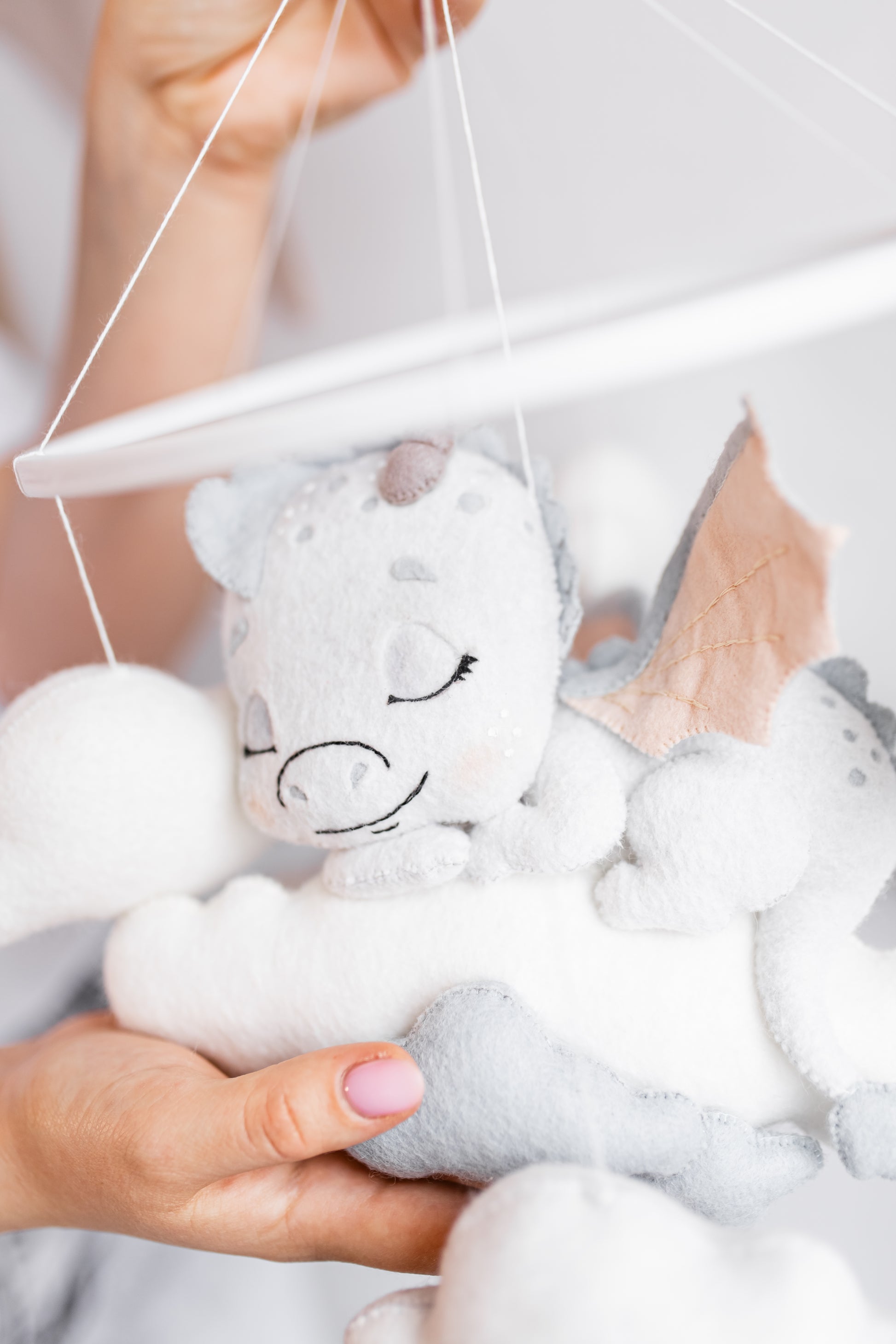 White plush dragon baby mobile with black accents held by a person against a white background