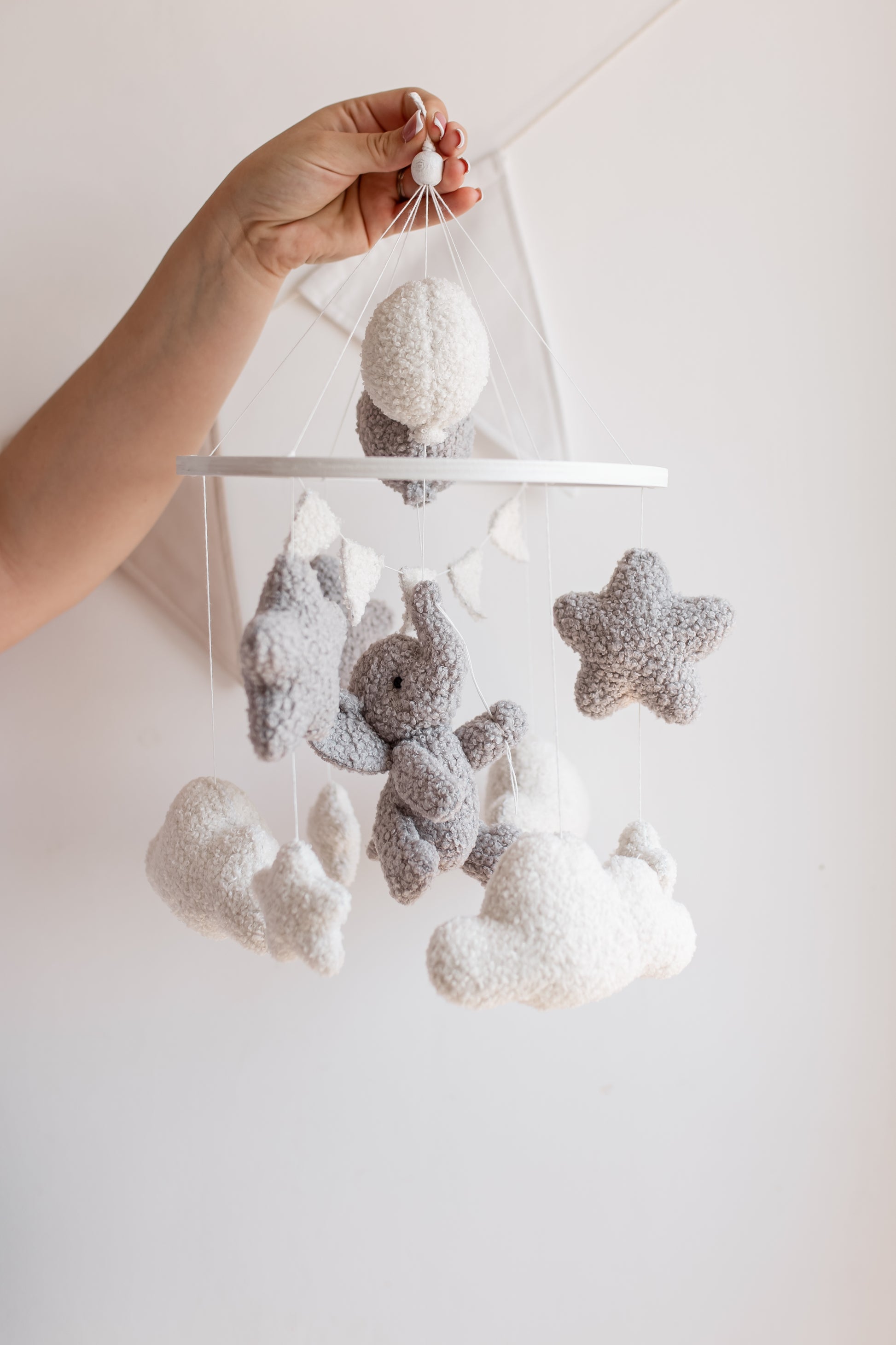 Baby mobile with stars, clouds, and a elephant toy hanging from a white rod against a light background.