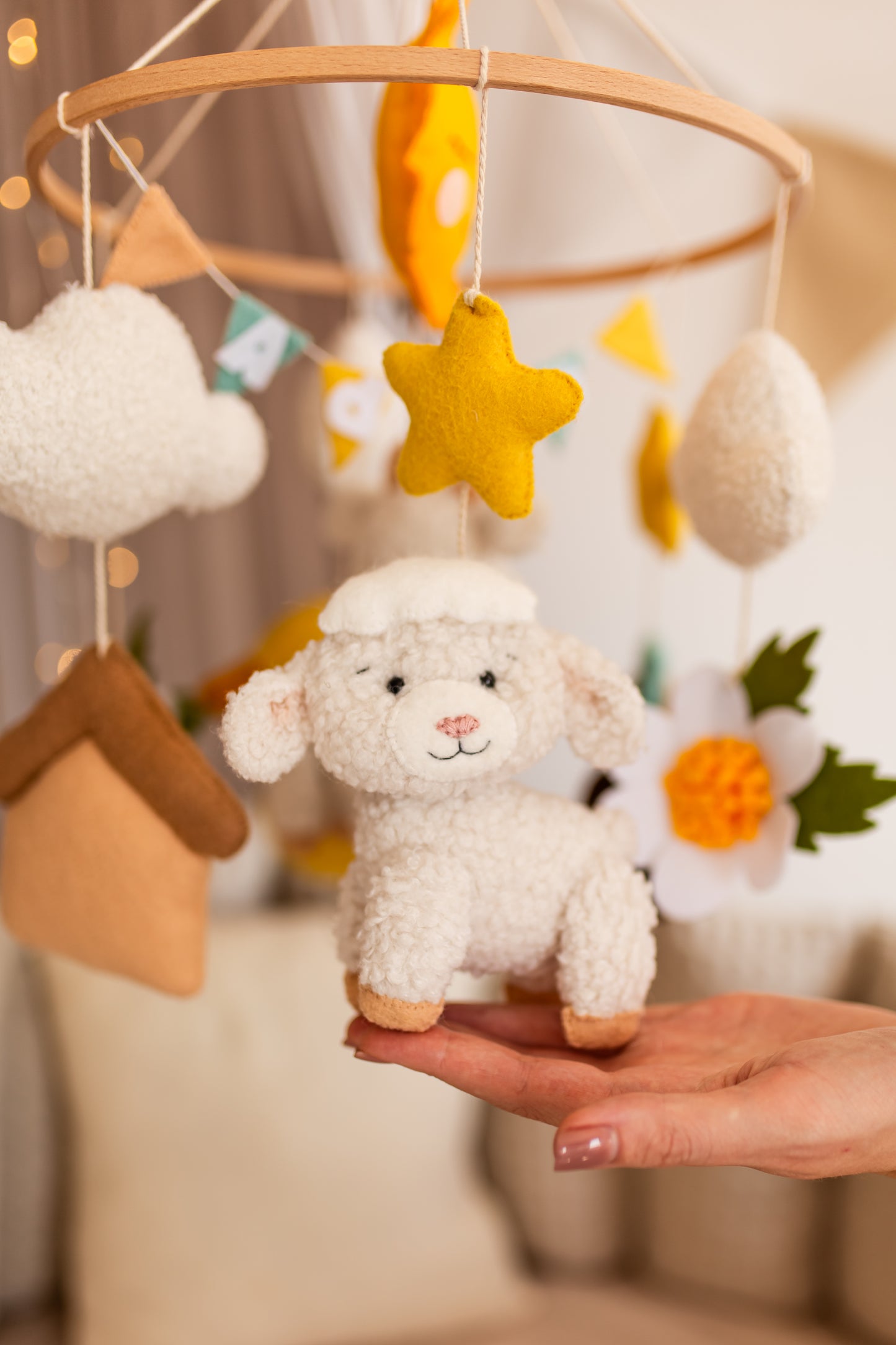 Baby mobile with plush lamb toy held by a hand against a blurred background
