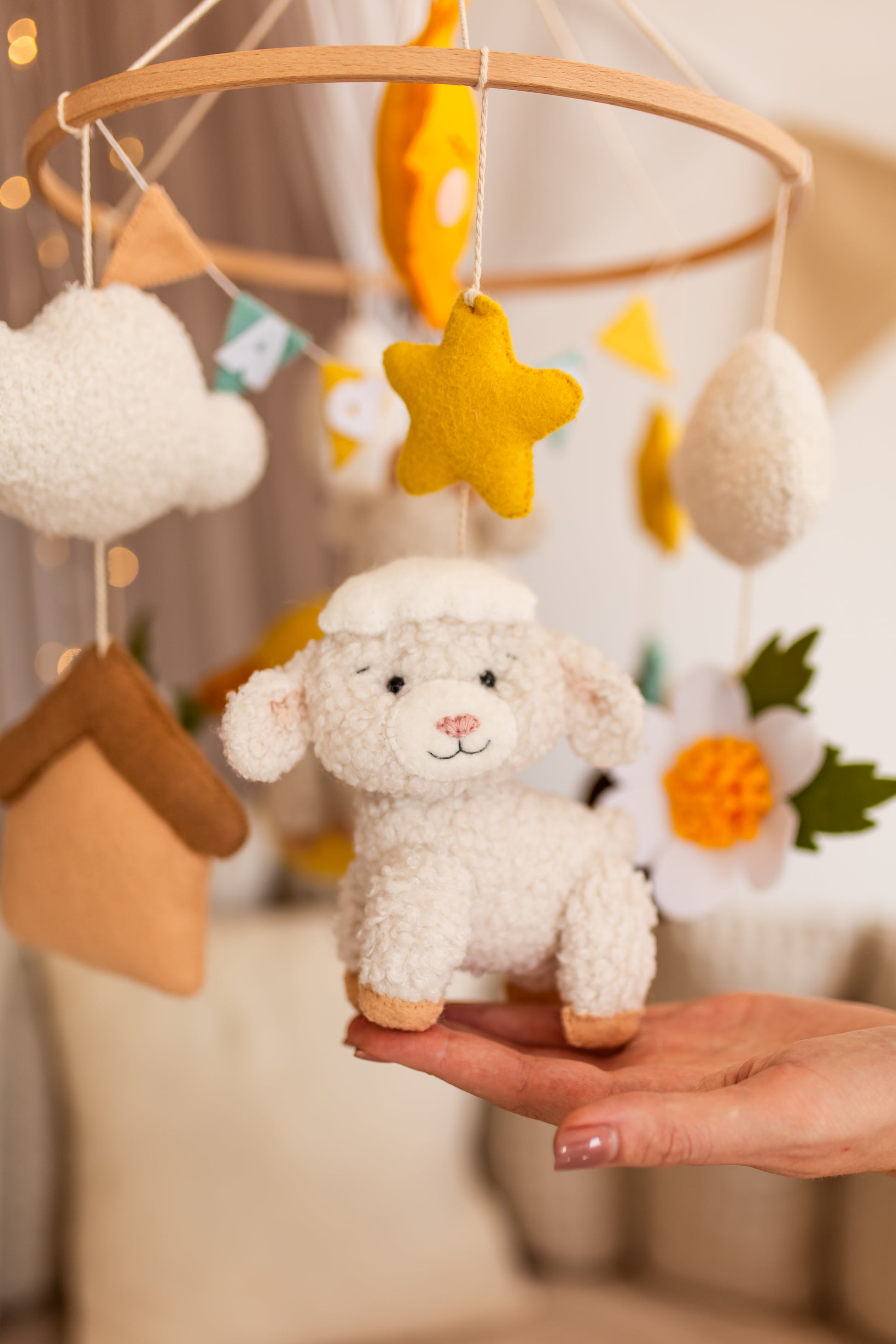 Baby mobile with plush lamb toy held by a hand against a blurred background