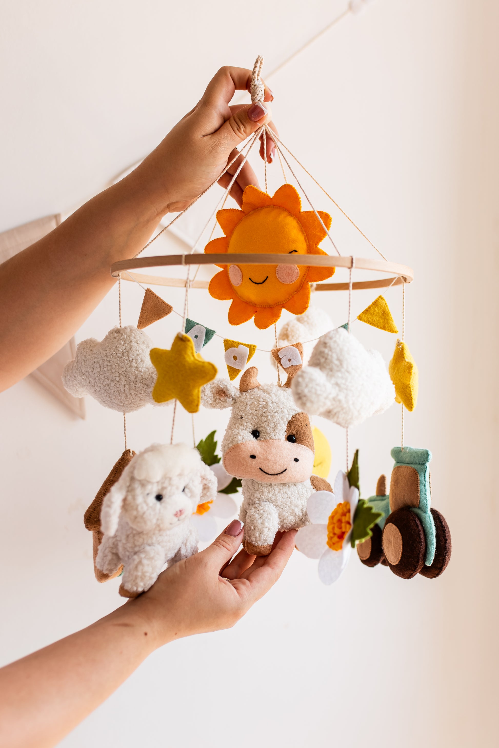 Children's mobile with plush animals and decorative elements held by a hand against a light background