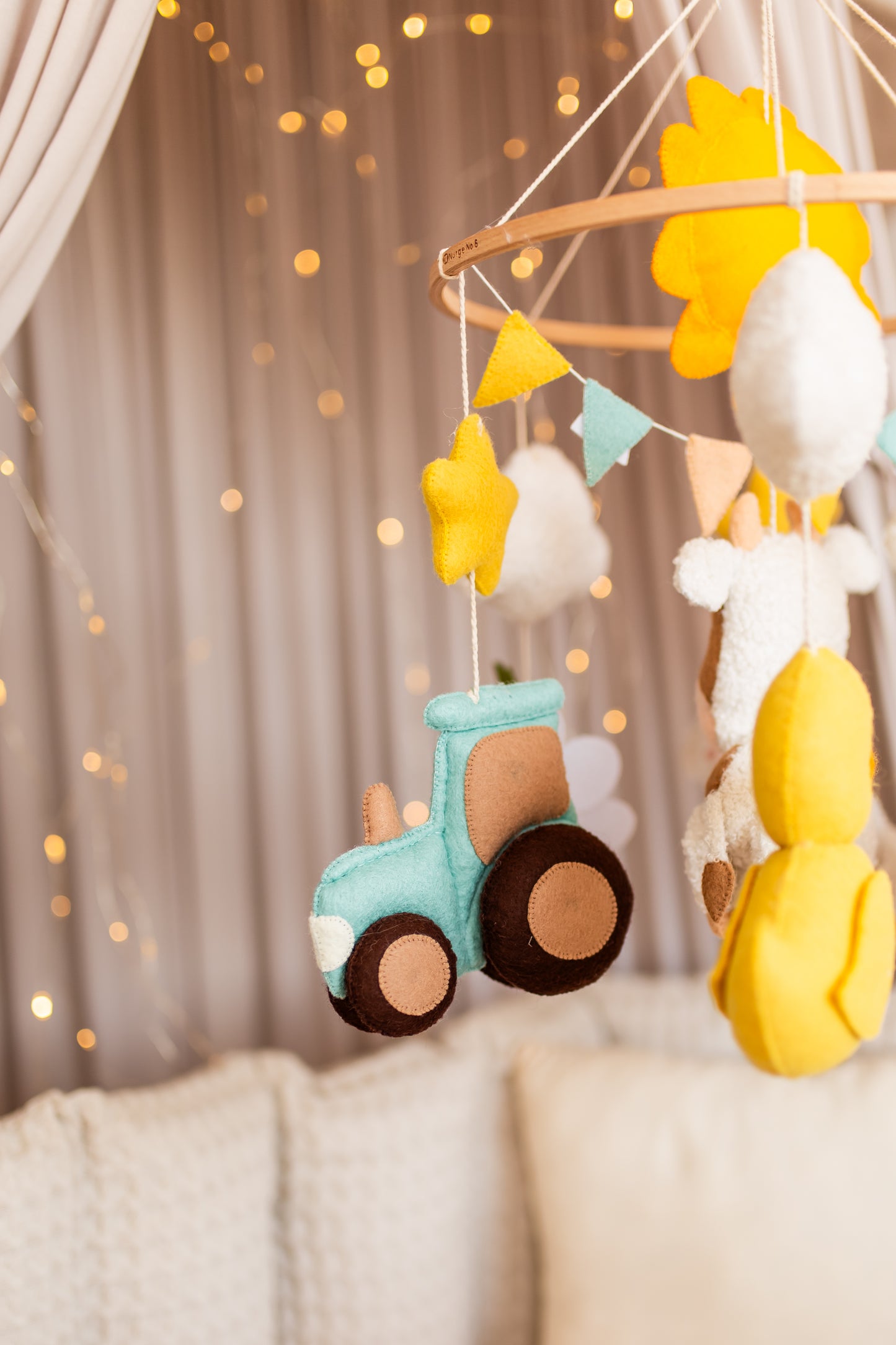 Baby mobile with colorful felt shapes and a toy tractor against a soft focus background