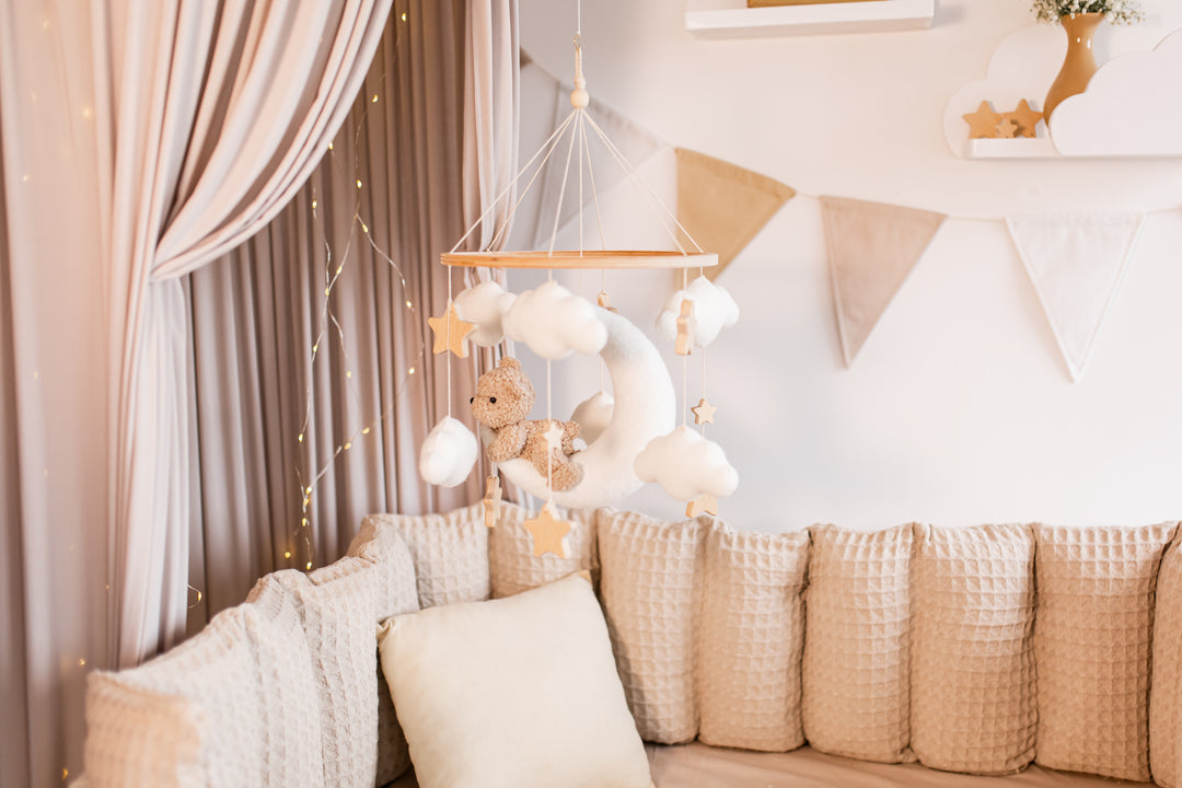 Decorative mobile with teddy bear and plush moon hanging above a sofa in a nursery.