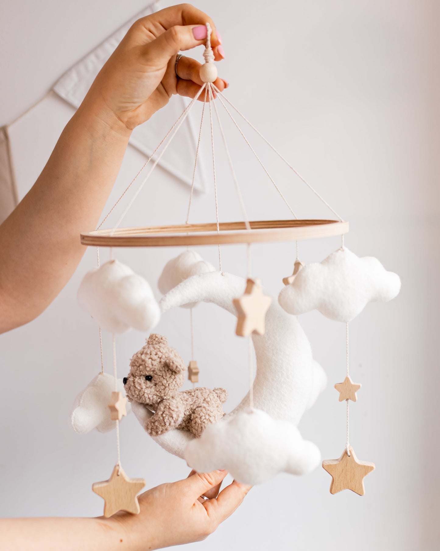 Baby mobile with teddy bear and stars held by a hand against a light background