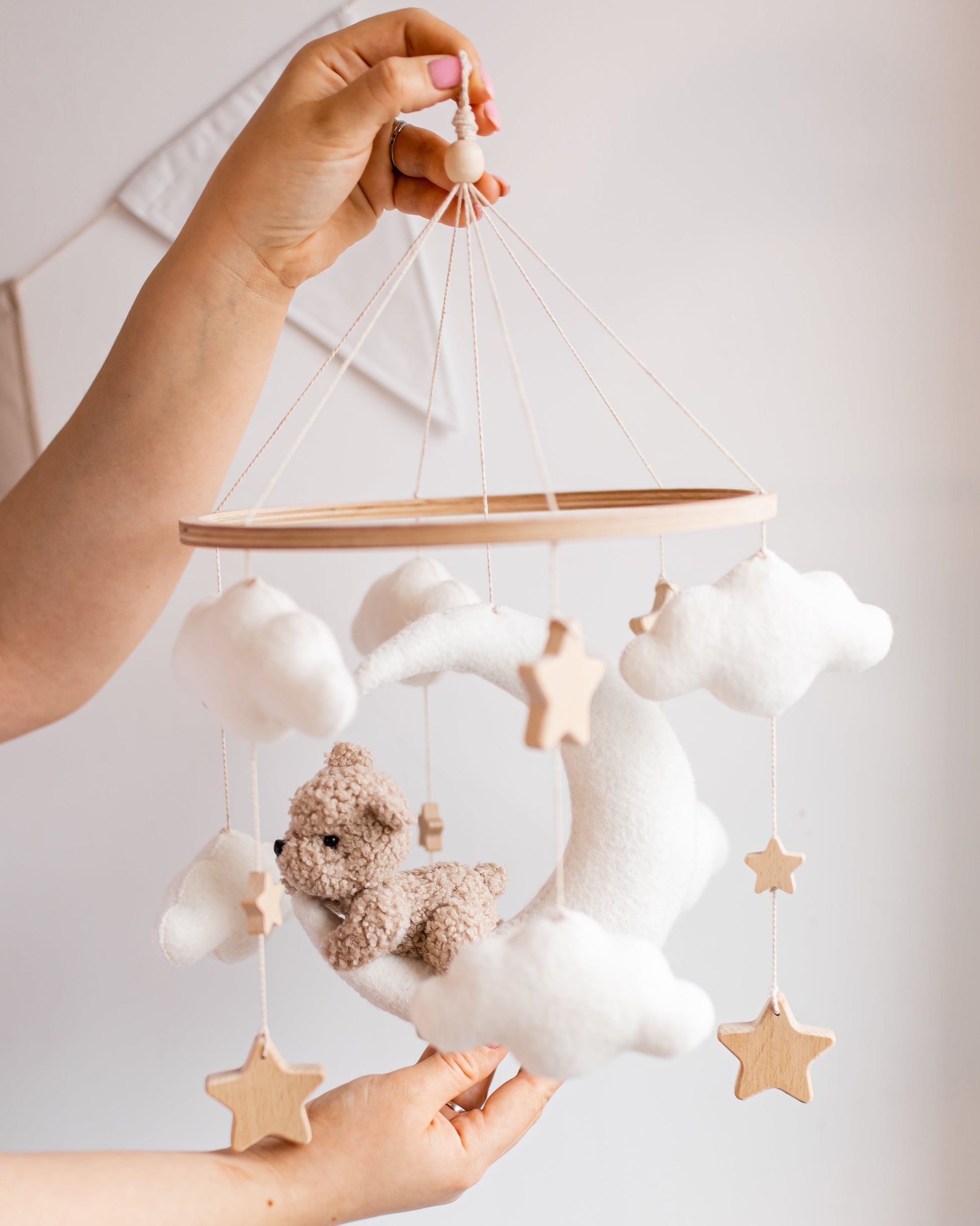 Baby mobile with teddy bear and stars held by a hand against a light background