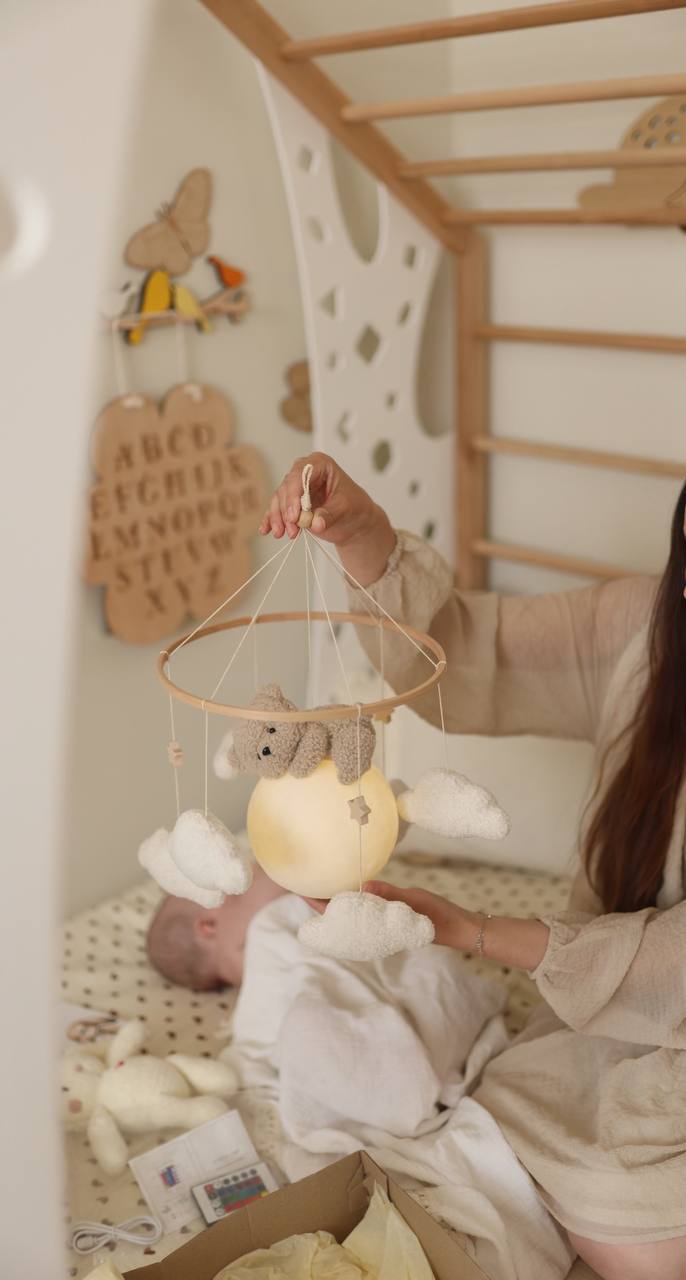 Baby in crib with mobile and toys, held by a person
