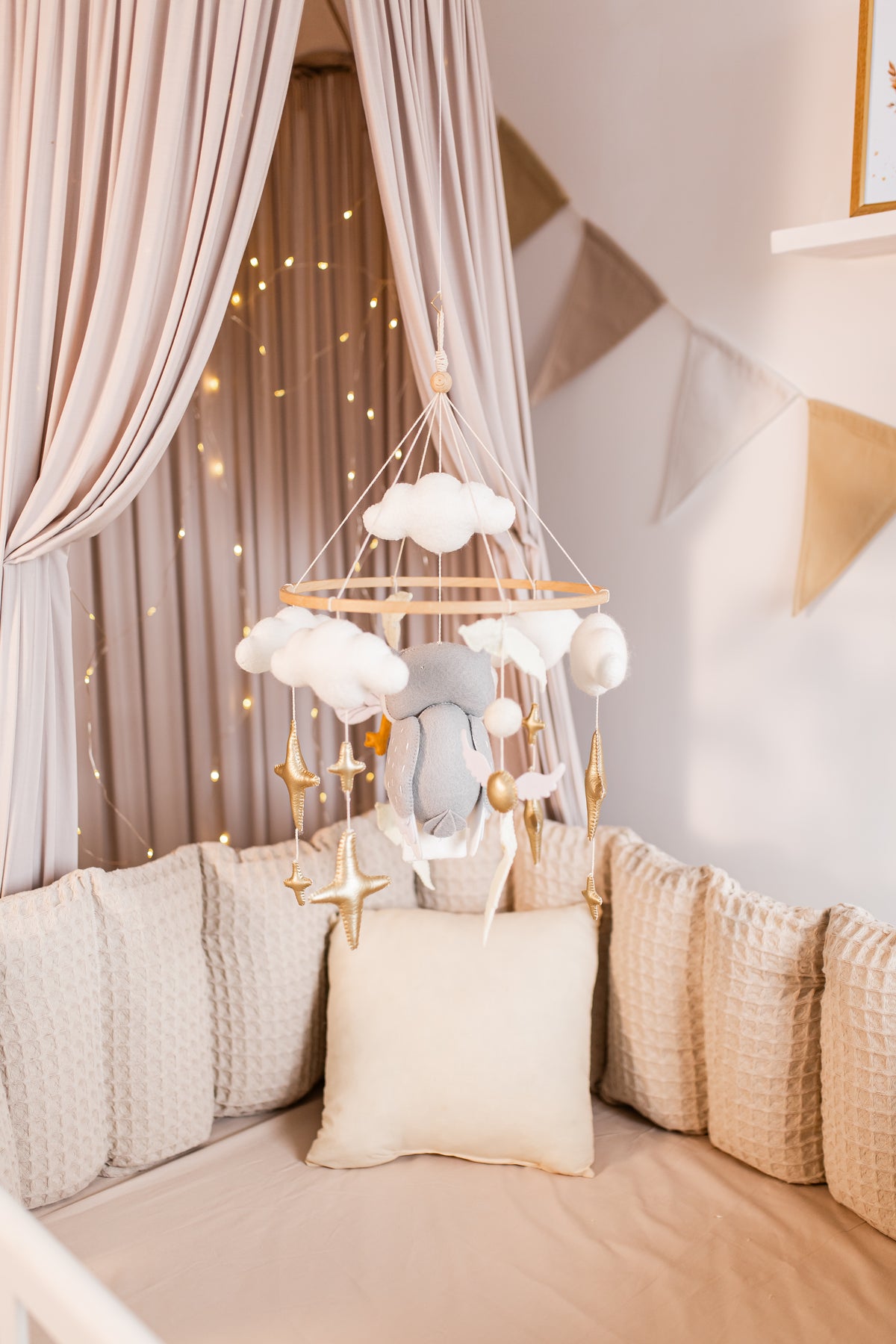 Decorative hanging mobile with clouds and stars above a crib with soft bedding.