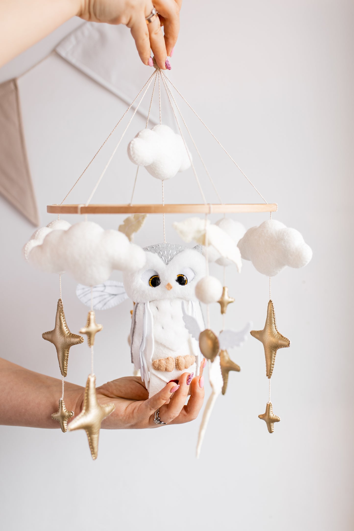 Baby mobile with clouds, stars, and a baby owl held by a person against a white background
