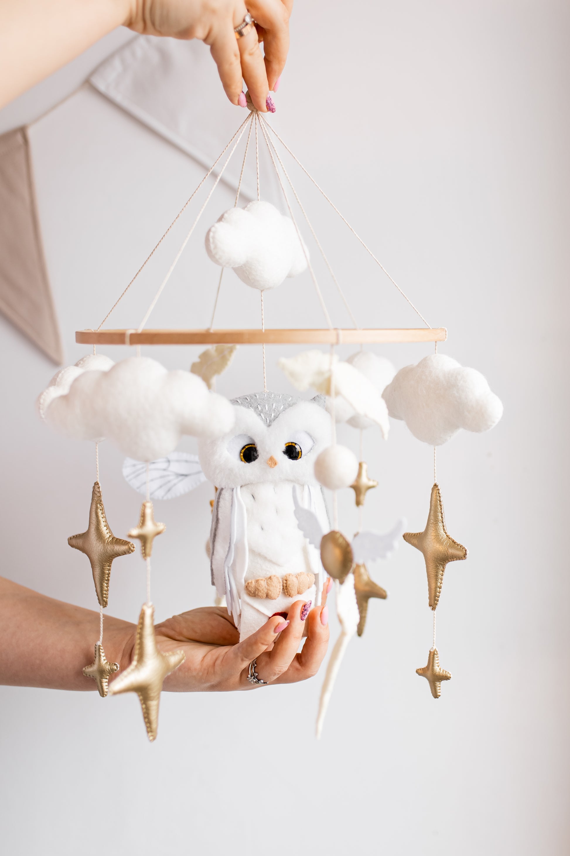 Baby mobile with clouds, stars, and a baby owl held by a person against a white background