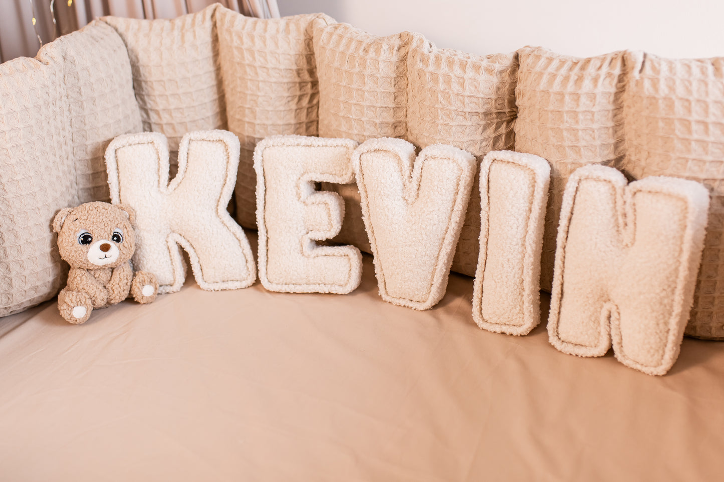 Beige 'KEVIN' letter pillows with a teddy bear on a beige surface
