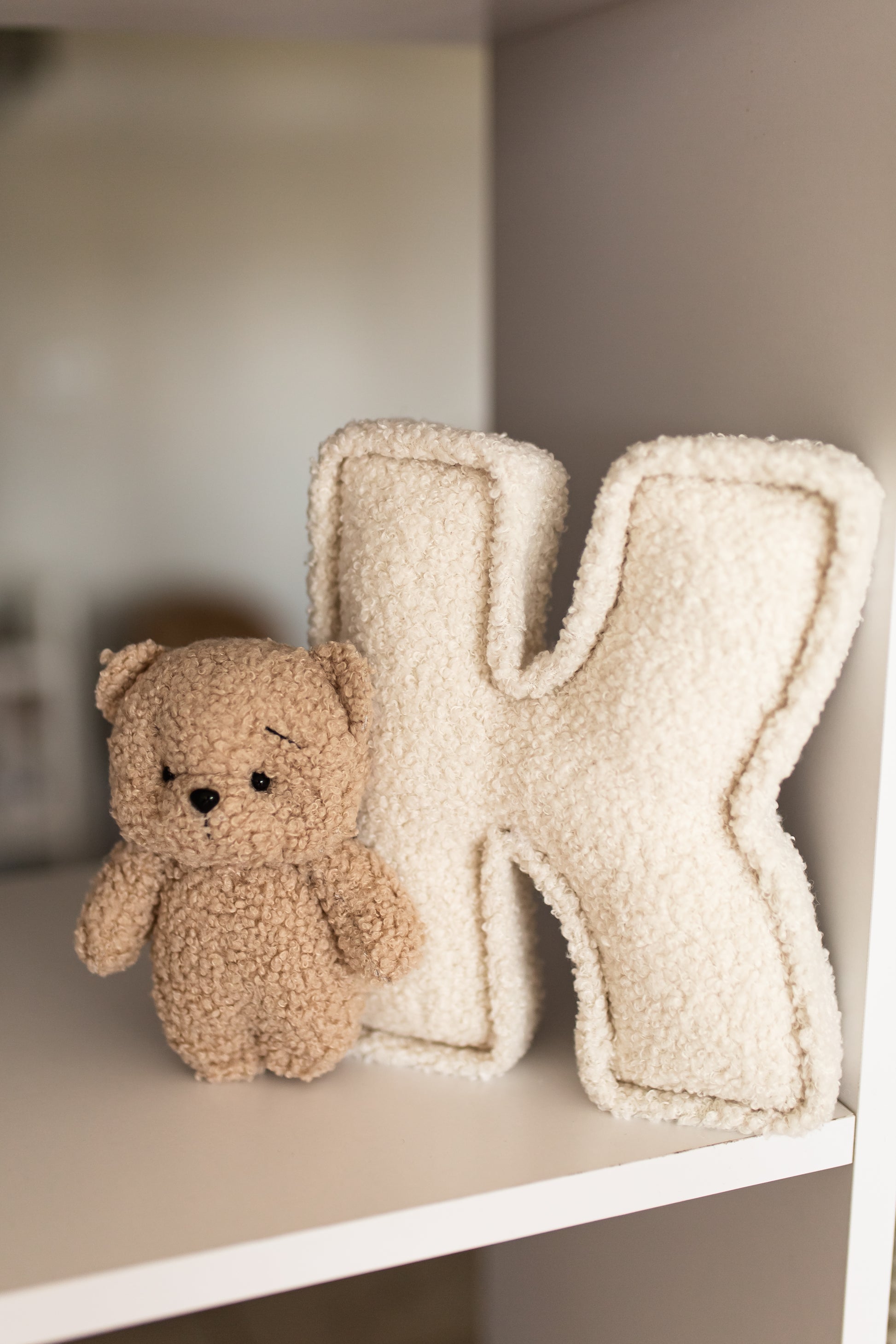 Small teddy bear next to a large letter 'K' on a shelf.