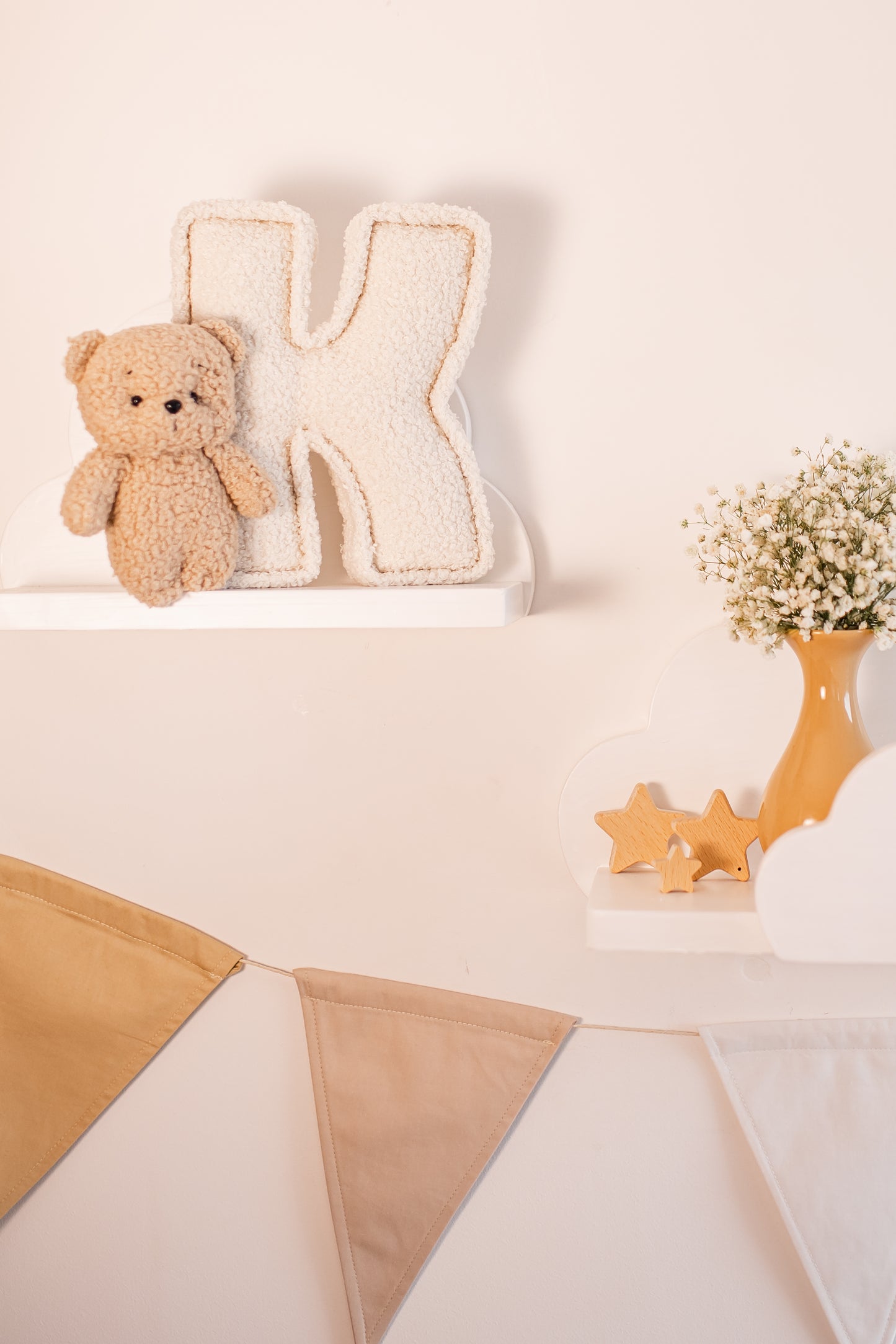 Decorative shelf with a teddy bear, letter 'K', and small plants on a light background