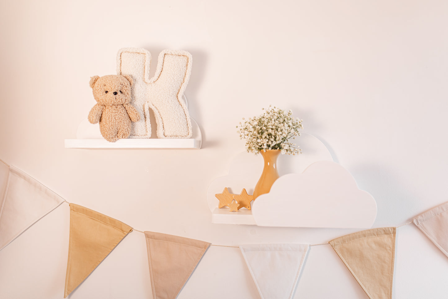 Decorative setup with a teddy bear, letter 'K', and flowers on a shelf against a light background.