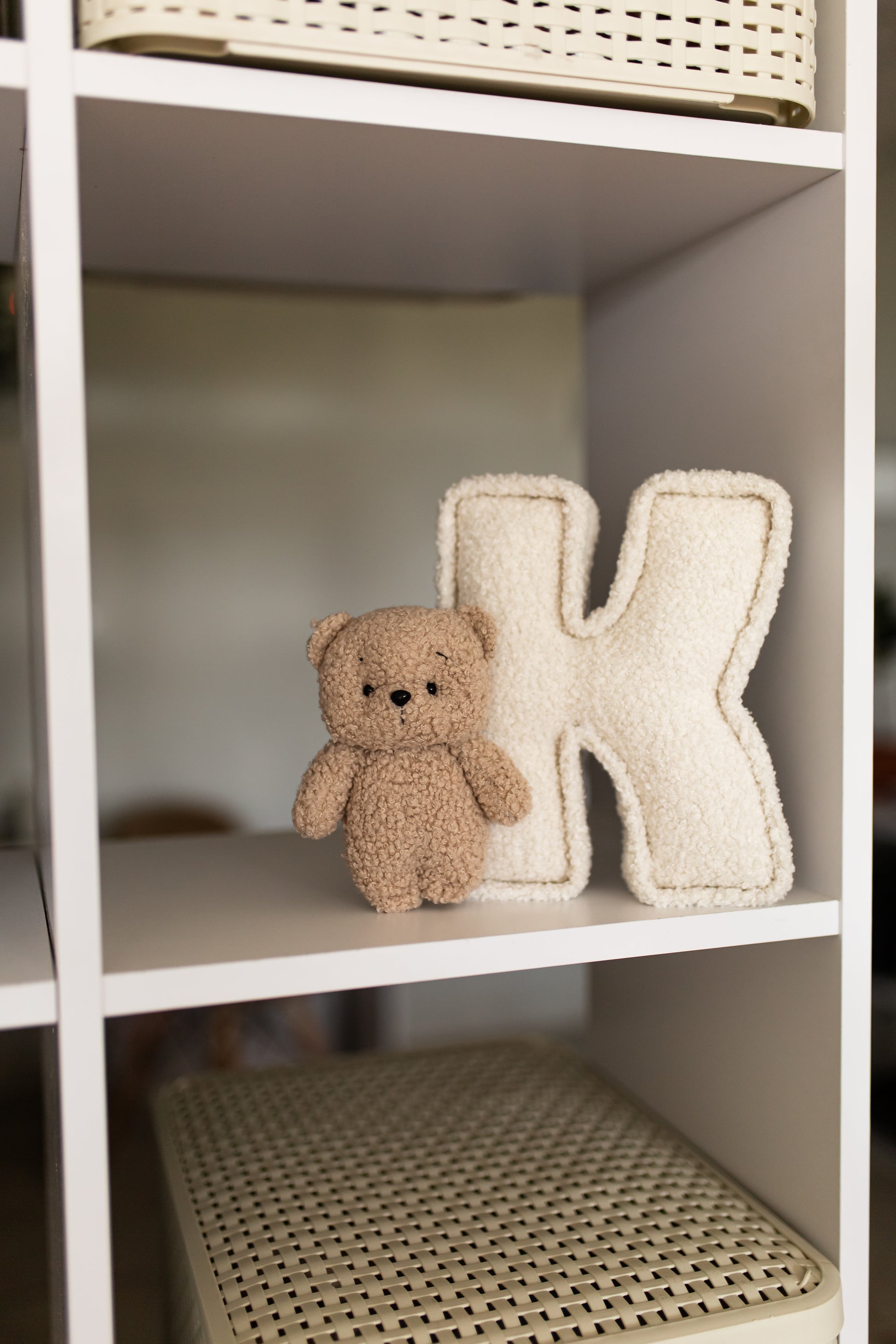 Small teddy bear and decorative letter 'K' on a white shelf.