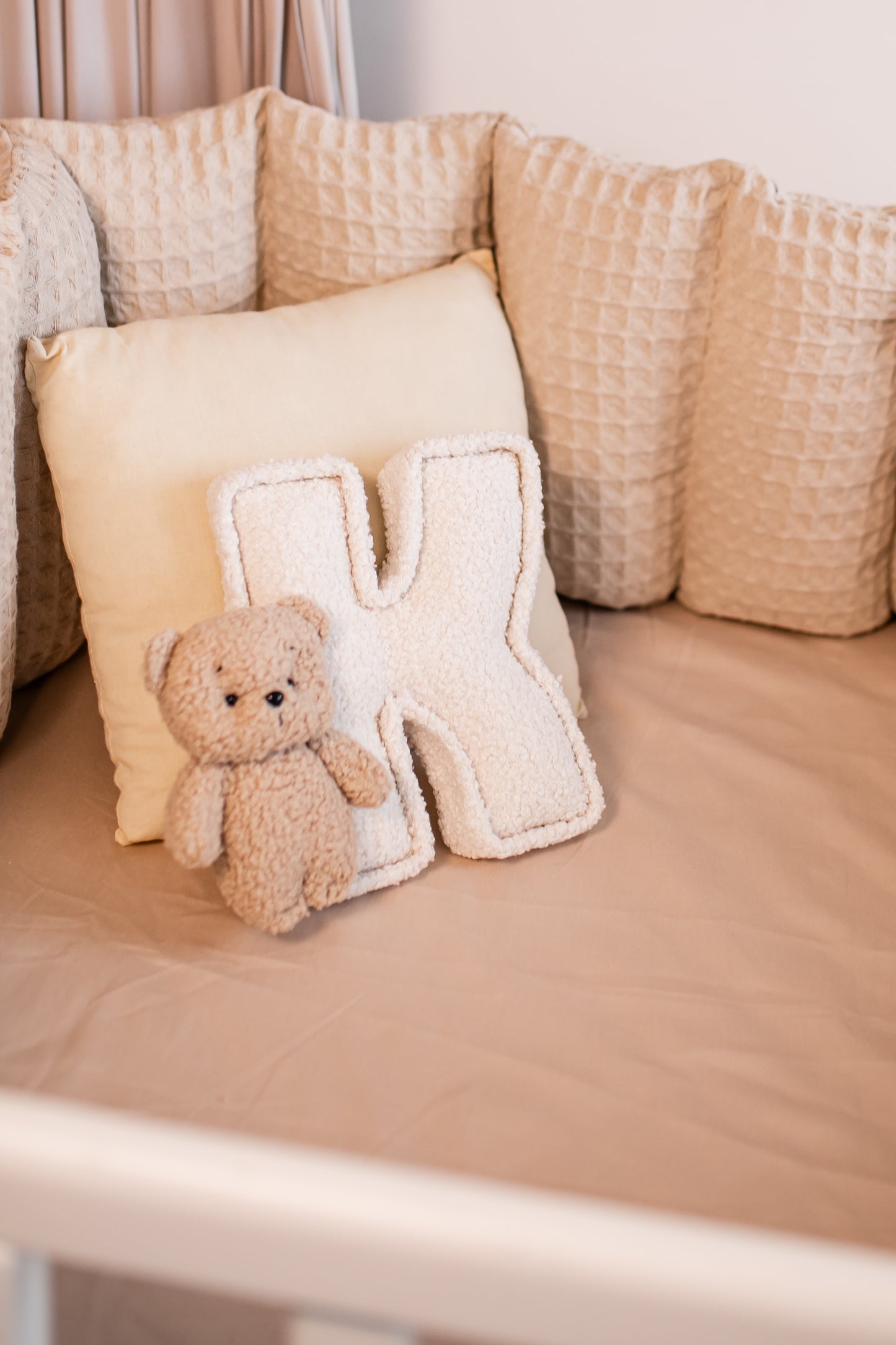 Beige teddy bear and letter 'K' pillow on a beige cushion