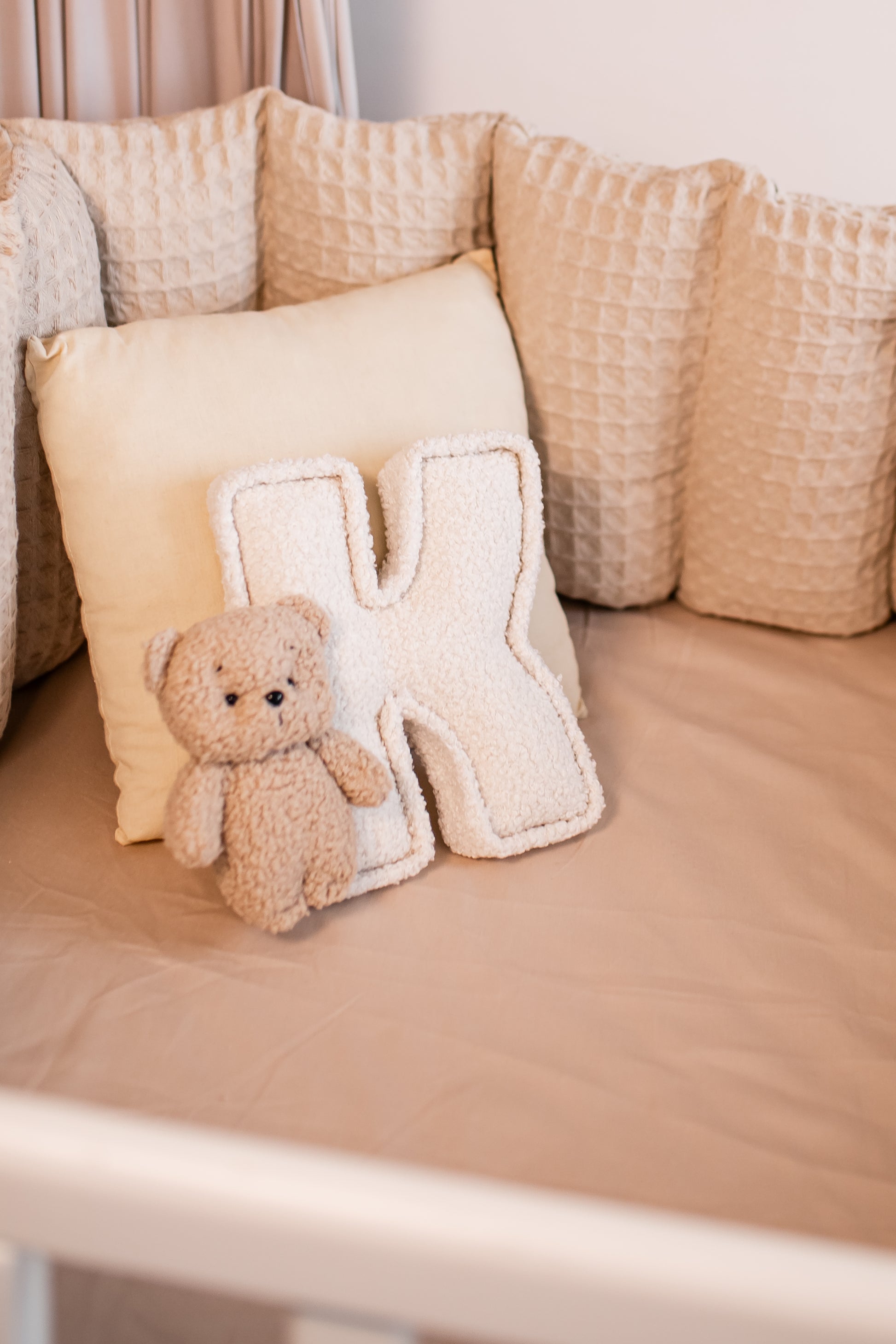 Beige teddy bear and letter 'K' pillow on a beige cushion