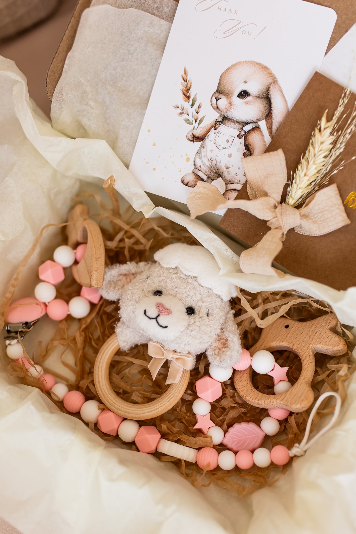 Baby teething ring and toy set with a card featuring a baby rabbit design, on a soft fabric background.