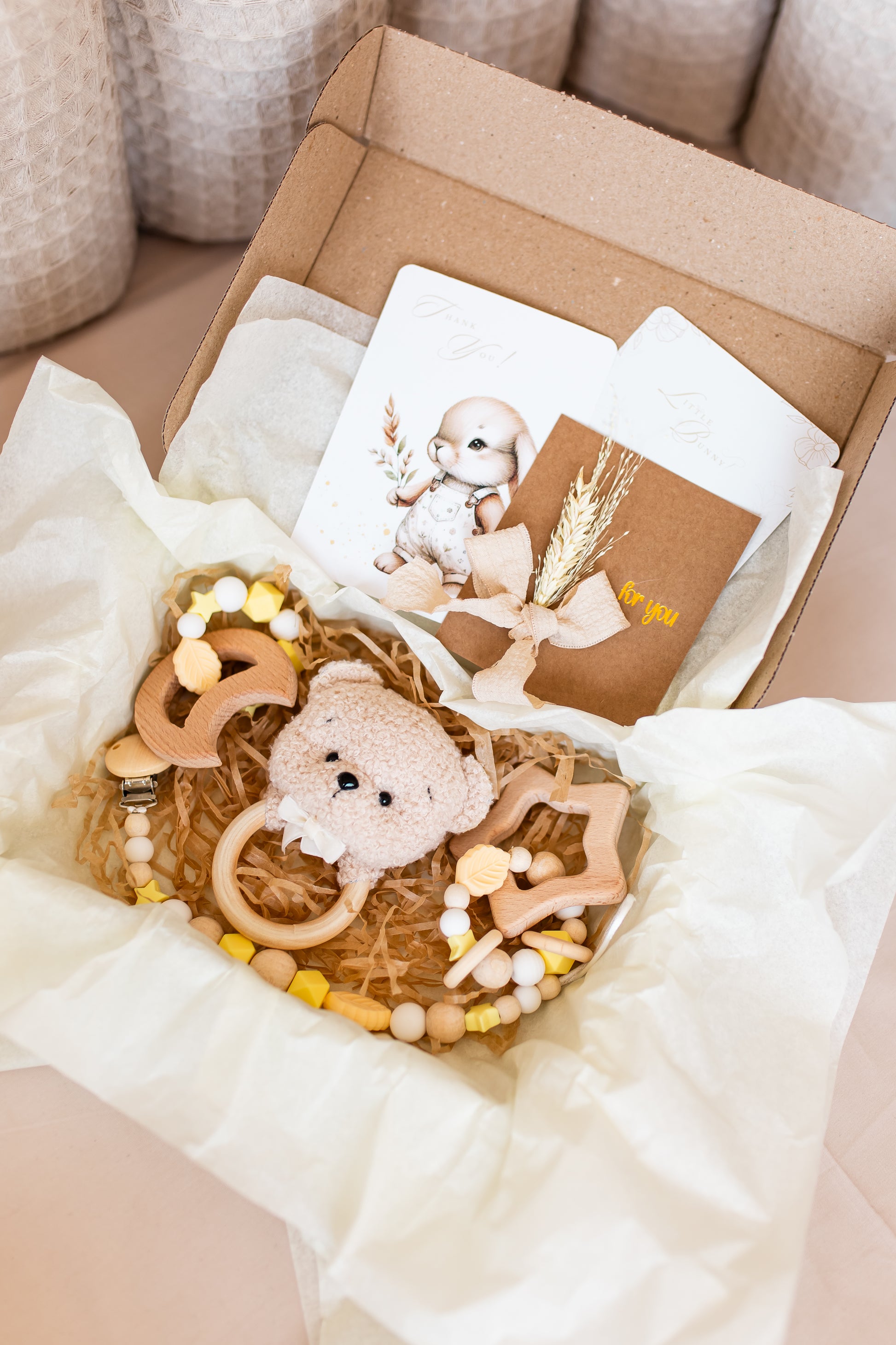 Baby teething toy with wooden elements and a teddy bear in a box with a card.
