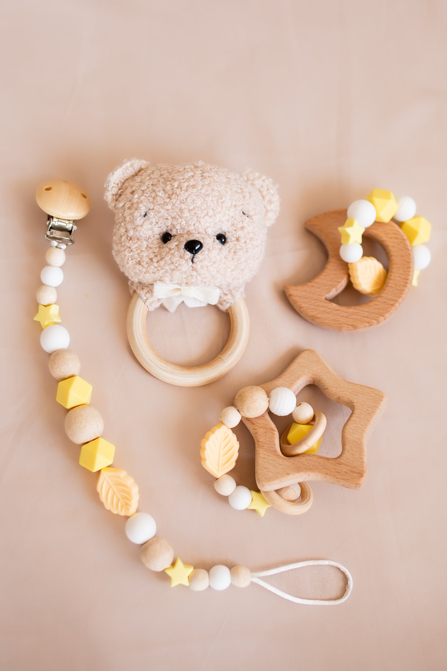 Collection of baby toys including a teddy bear, teething ring, and beaded necklace on a beige background
