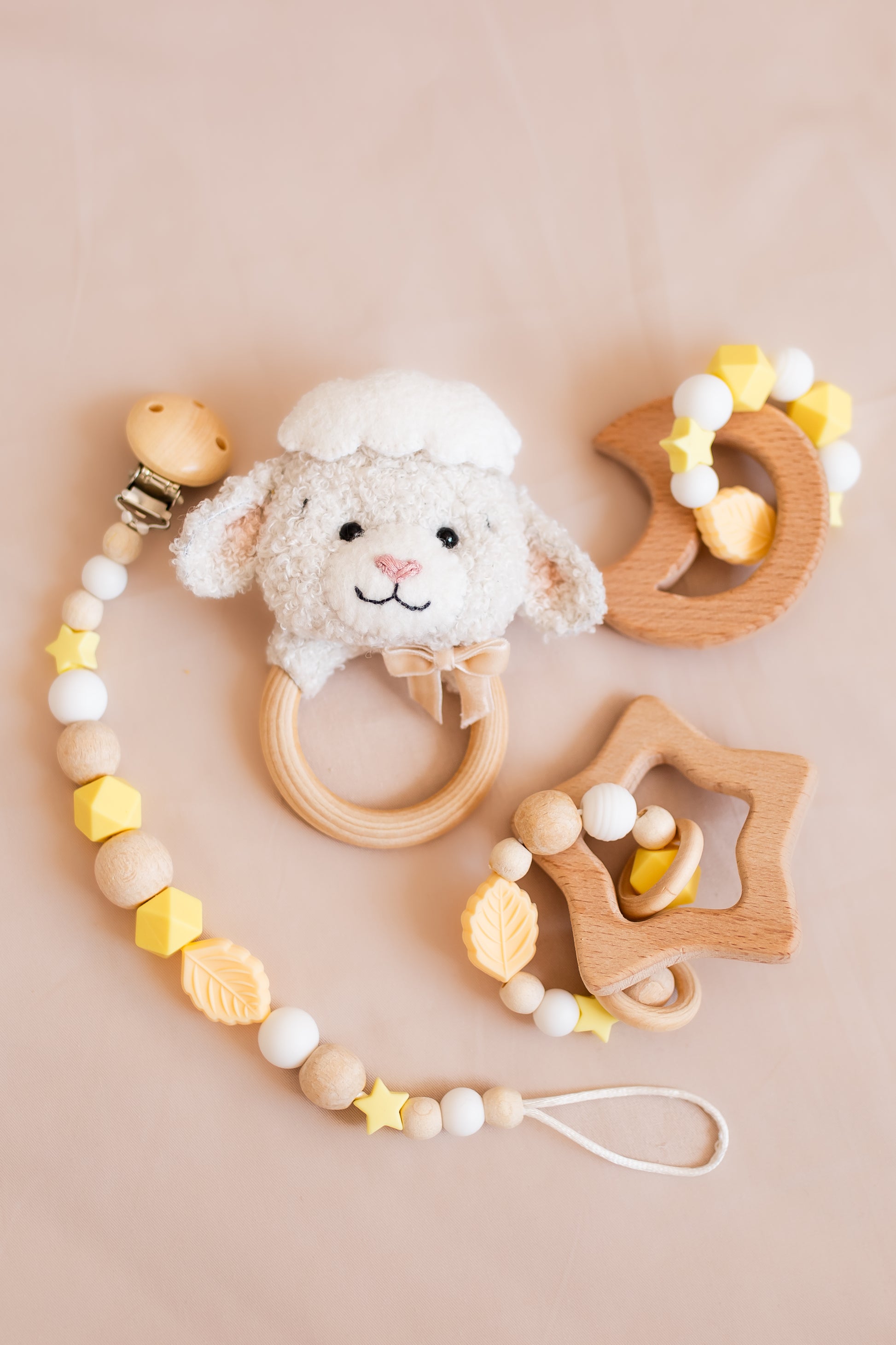 Set of baby toys including a sheep rattle, wooden star, and teething ring on a beige background
