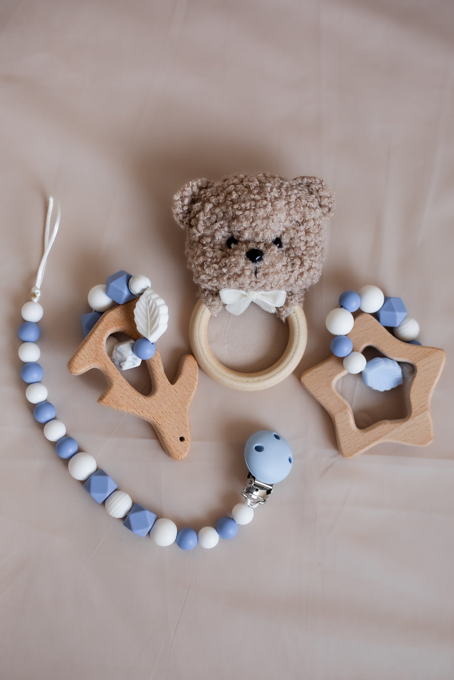 Baby teething toy set with bear rattle, star and animal-shaped wooden toys on a beige background.