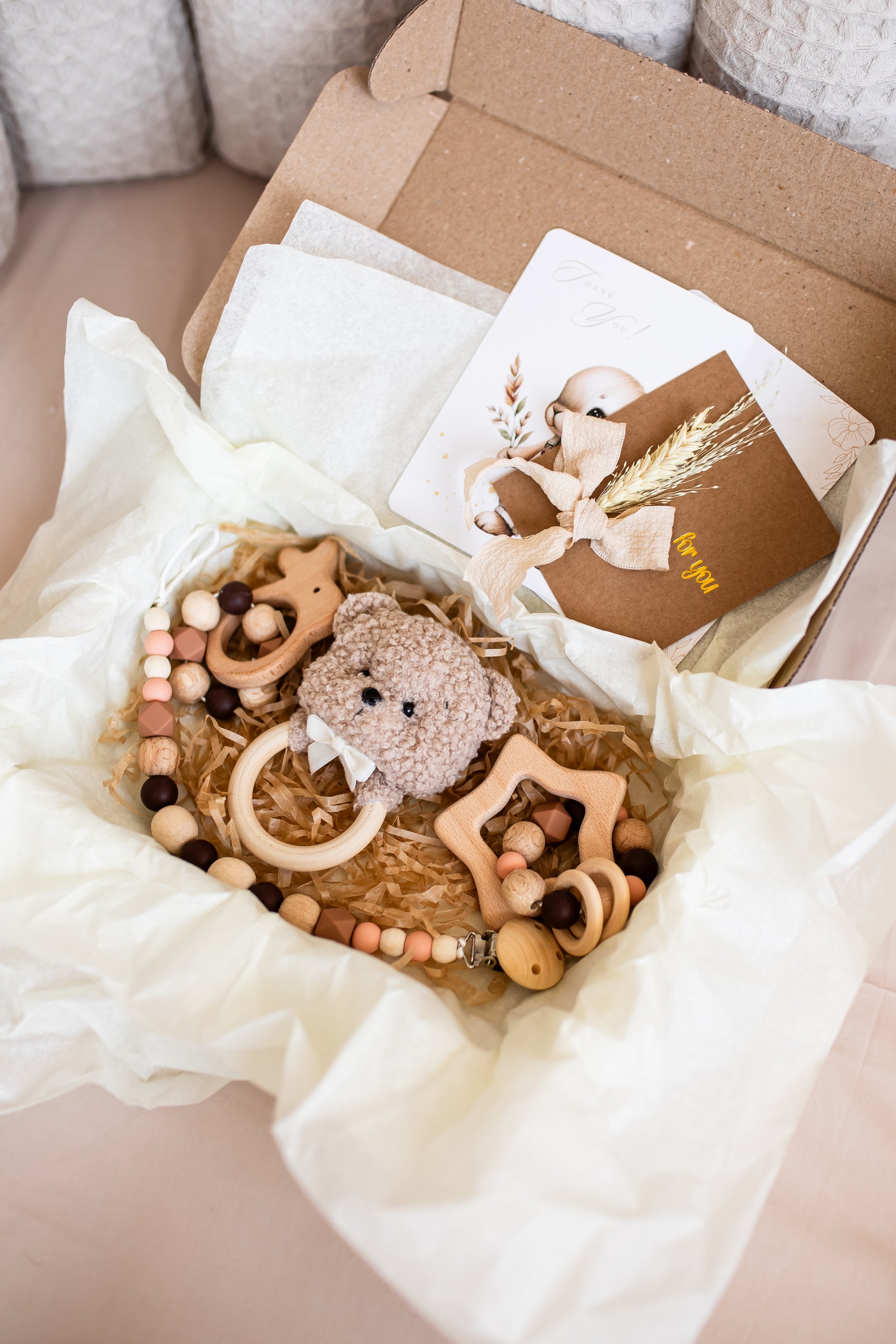 Baby teething toys and a card in a box with white tissue paper