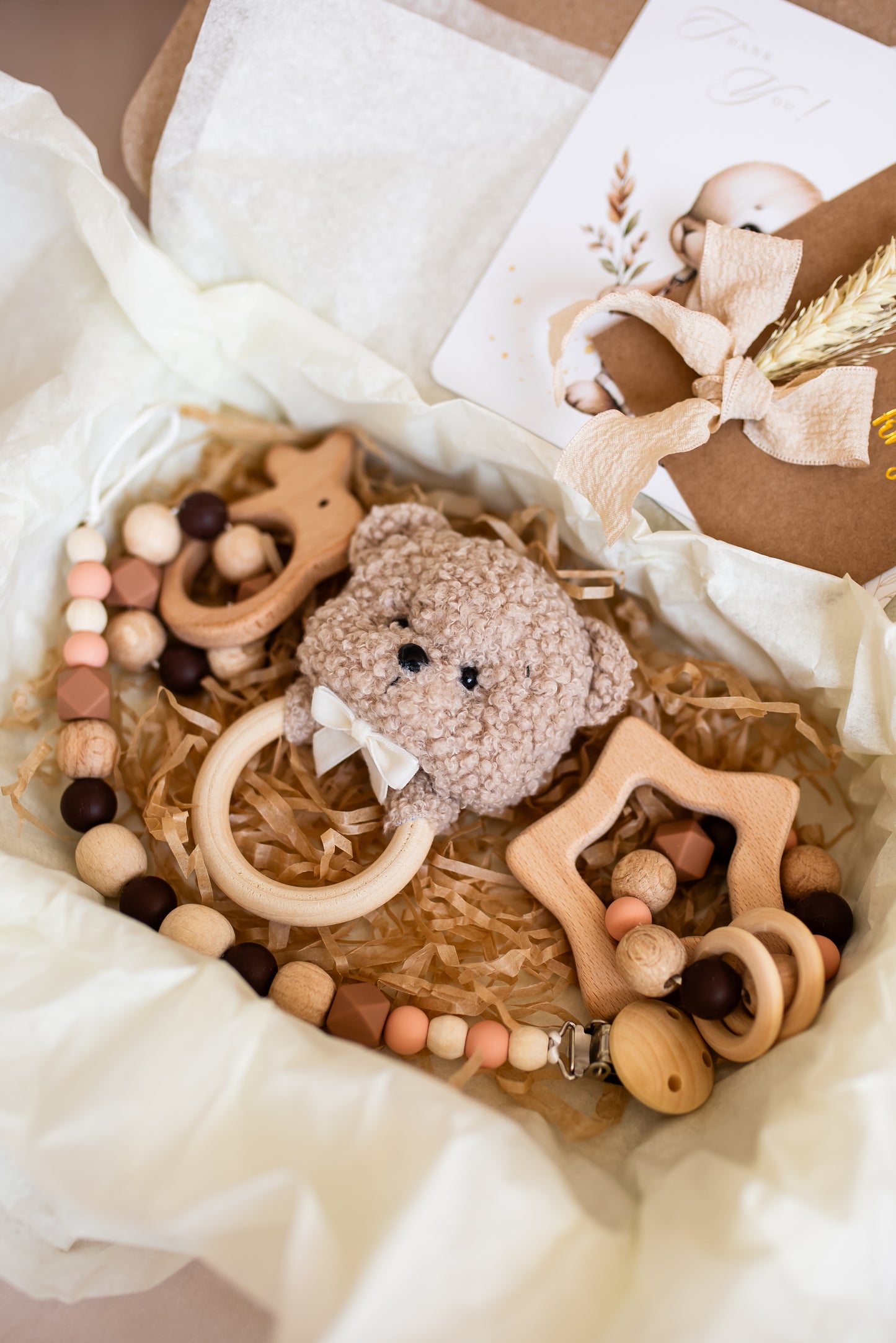 Collection of baby toys including a plush toy, wooden rings, and beads in a decorative box.