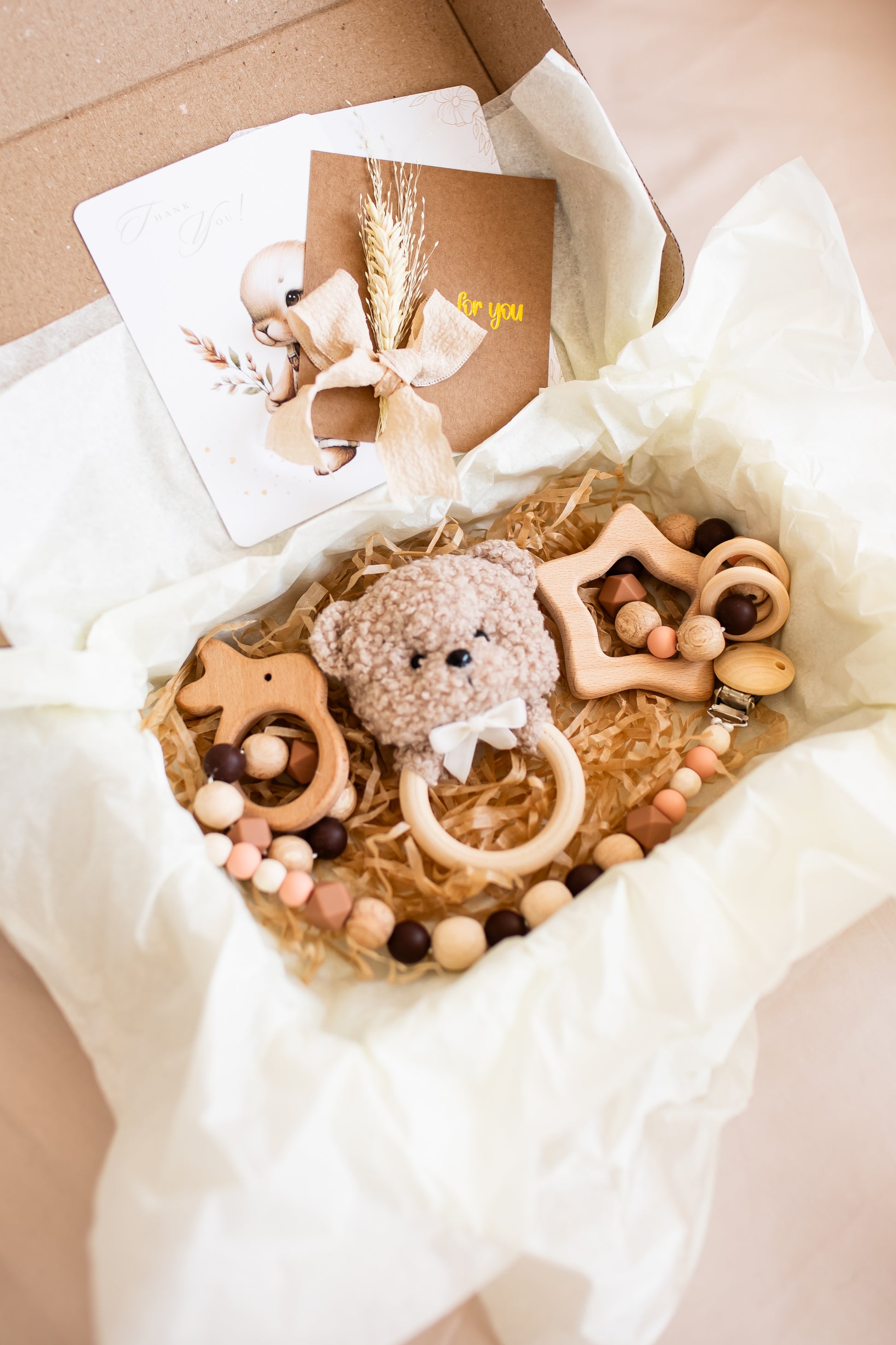 Wooden baby toys and a teddy bear in a box with a card on a light background