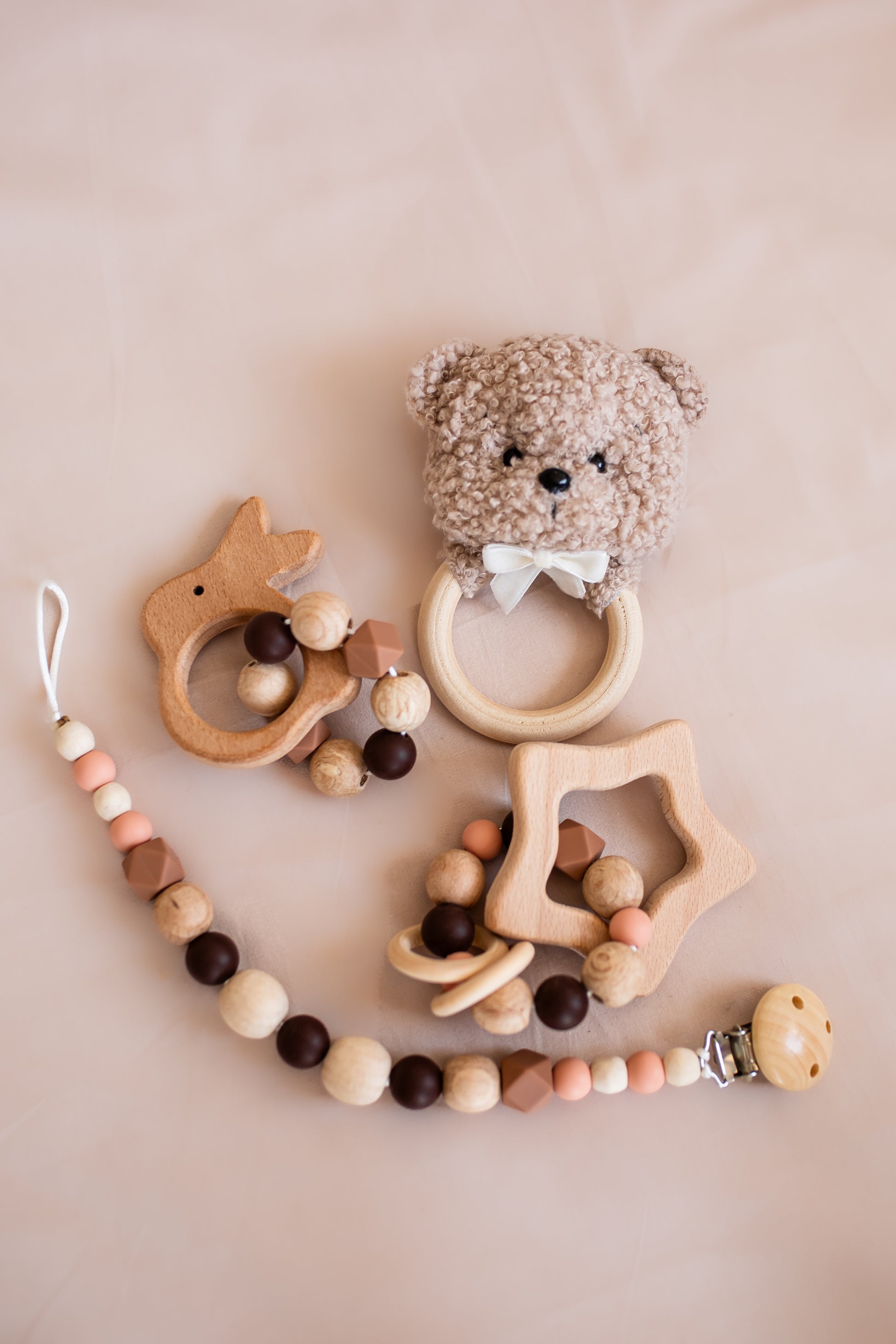 Set of baby teething toys including a bear rattle, star-shaped teether, and bead chain on a beige background.