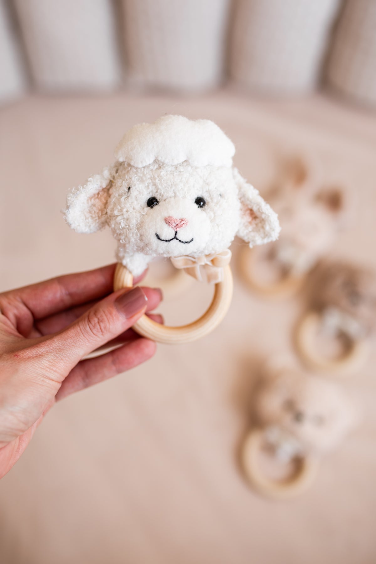 Hand holding a sheep-shaped teething ring with a blurred background