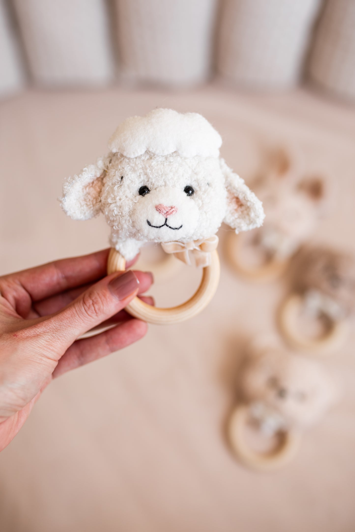 Hand holding a sheep-shaped teething ring with a blurred background
